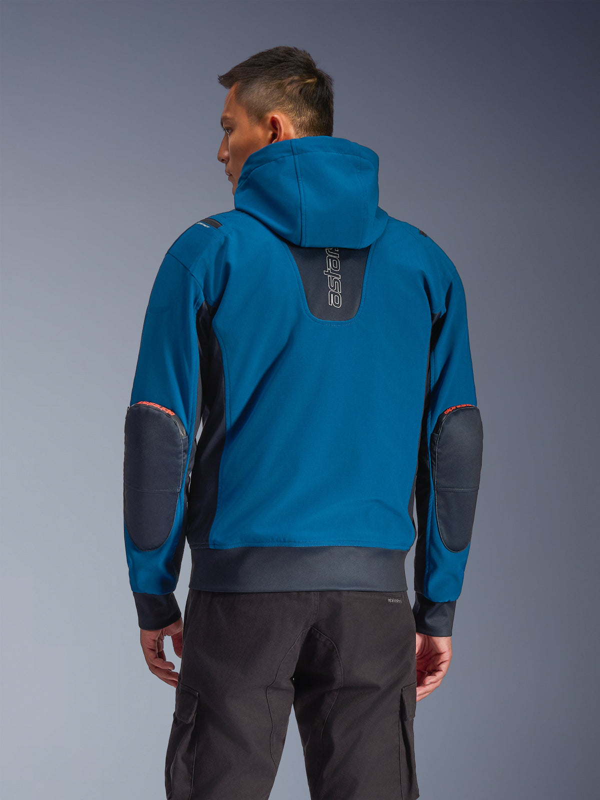 Alpinestars Moblast Waterproof Jacket, kolory Dark Petrol i Dark Navy, miejska bluza motocyklowa widoczna z tyłu, ze stałym kapturem, pionowym logo „astars” w górnej części pleców, ciemnymi wzmocnionymi łatami na łokciach oraz elastycznym pasem i mankietami, nowoczesna techniczna odzież motocyklowa