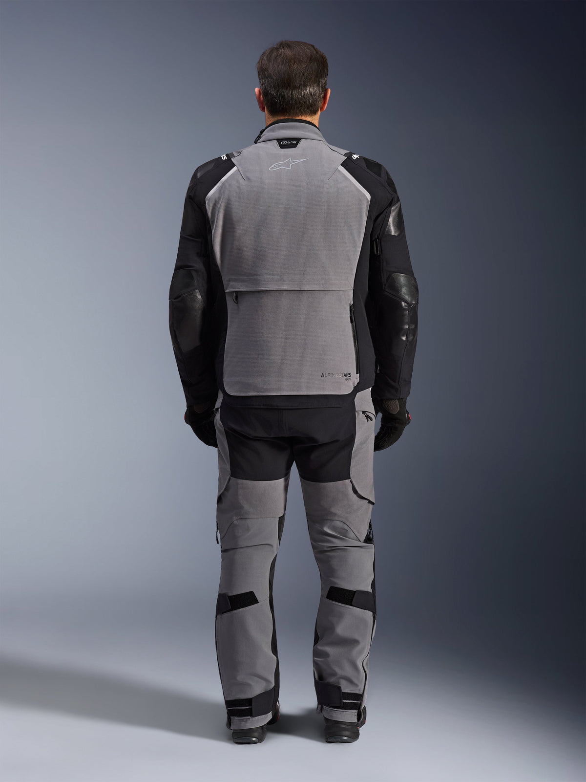 Alpinestars Andes Pro Drystar® XF Jacket, Dark Gray Black, back view of a rider wearing matching pants, adventure touring motorcycle jacket featuring a large gray back panel, black articulated sleeves with protection, and a rear storage compartment