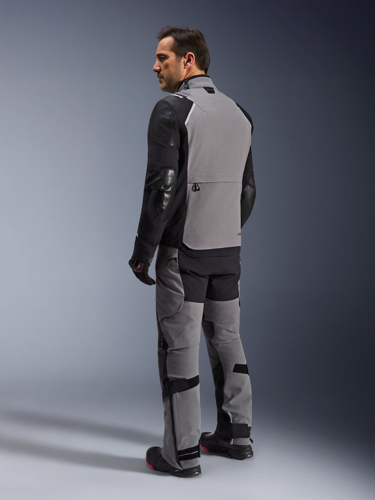Alpinestars Andes Pro Drystar® XF Jacket, adventure-touring motorcycle jacket in Dark Gray and Black, rear view on a model showing the large back panel and reinforced sleeves, paired with matching adventure pants, gloves, and boots