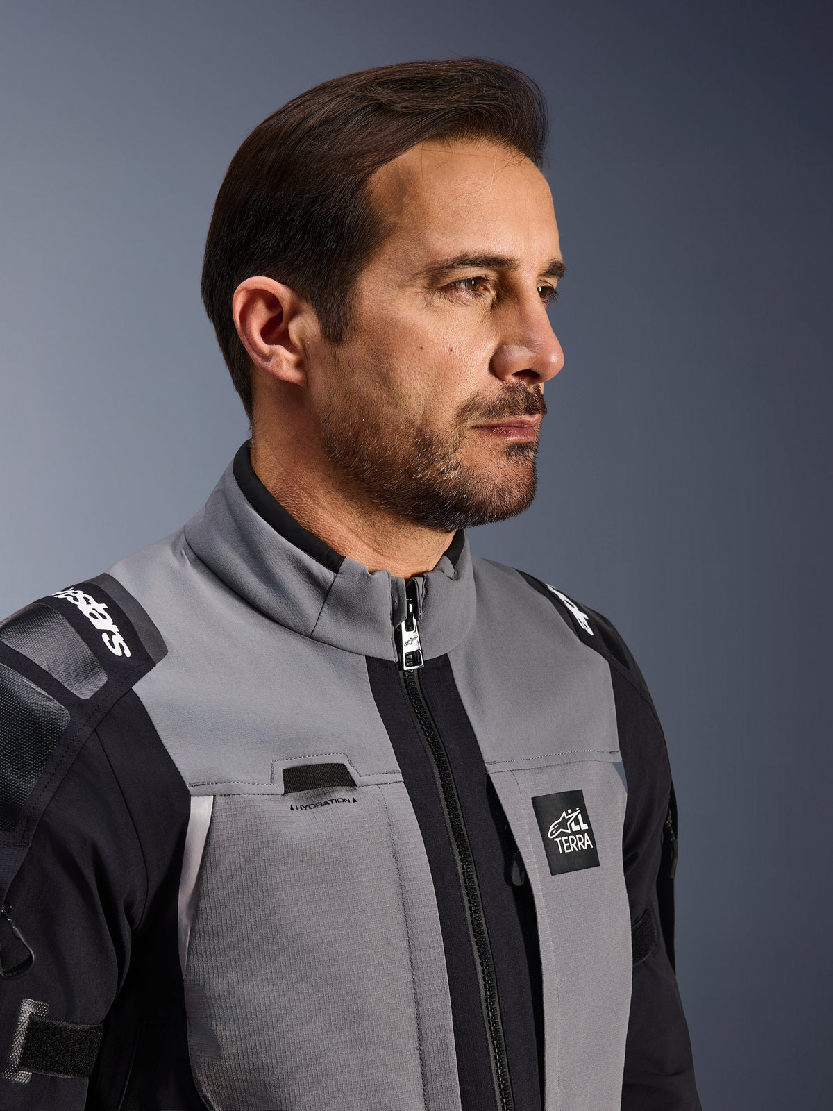 Alpinestars Andes Pro Drystar® XF Jacket, Motorcycle Adventure Jacket, Dark Gray and Black, close-up of the front torso and collar, featuring Terra branding and hydration routing detail, worn by a man in a studio setting