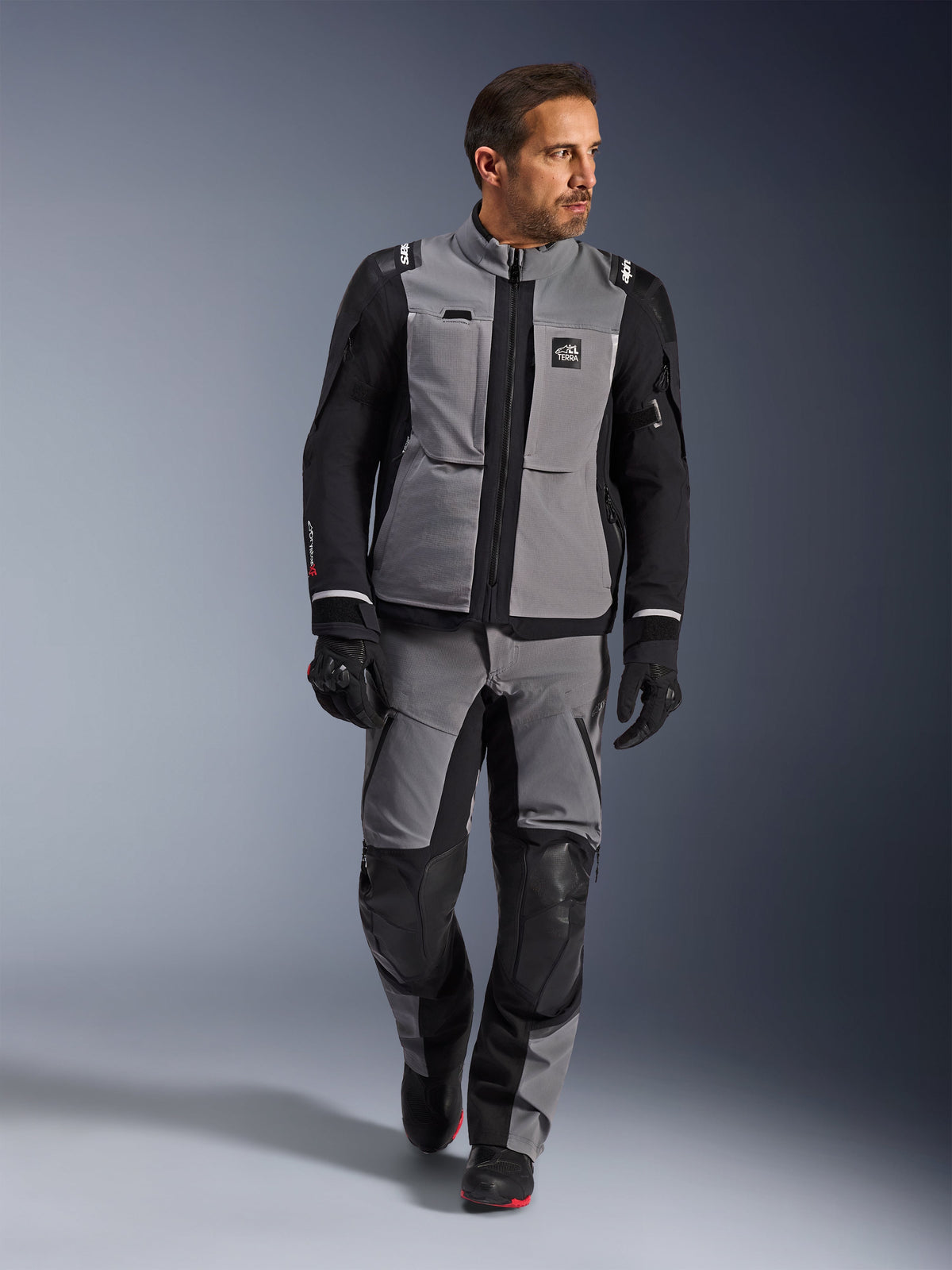 Male model wearing Alpinestars Andes Pro Drystar® XF Jacket in Dark Gray and Black, adventure motorcycle riding suit with matching pants and gloves, featuring a technical textile shell with 'All Terra' branding, complete gear for long-distance adventure touring