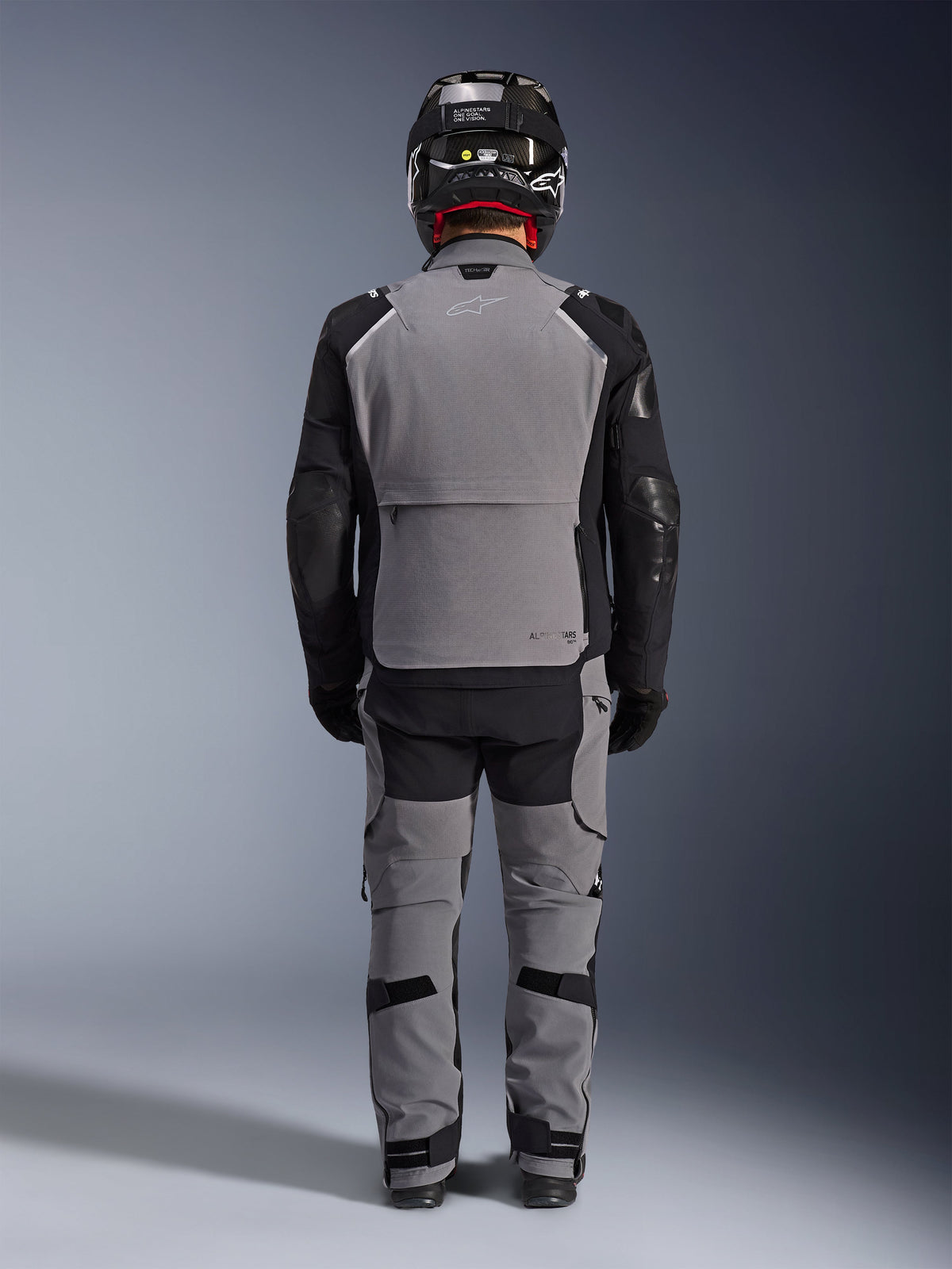 Alpinestars Andes Pro Drystar® XF Jacket, back view, Dark Gray and Black adventure touring gear, worn with matching gray and black pants, black carbon fiber helmet, and black gloves, featuring technical panels and reflective branding
