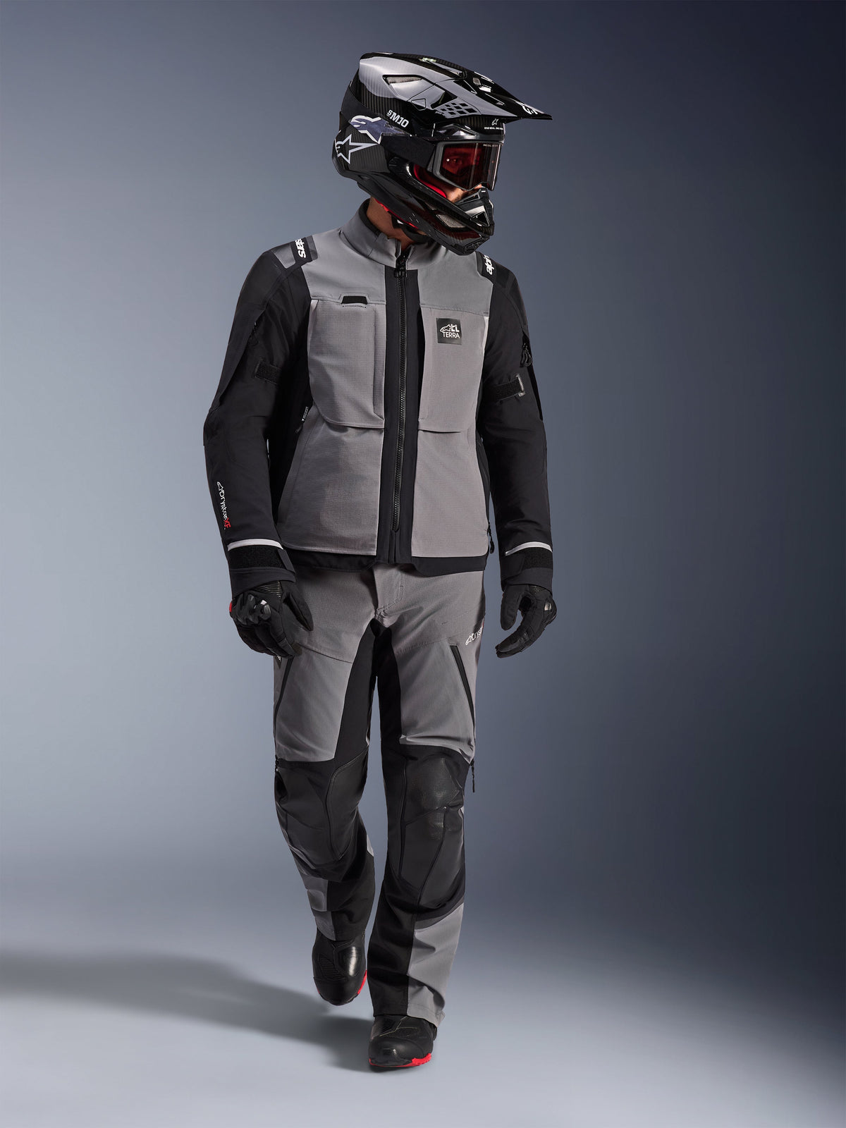 Adventure rider wearing Alpinestars Andes Pro Drystar® XF Jacket in Dark Gray and Black, matching adventure pants, black Alpinestars helmet with goggles, black gloves and boots, complete technical touring gear for long-distance riding