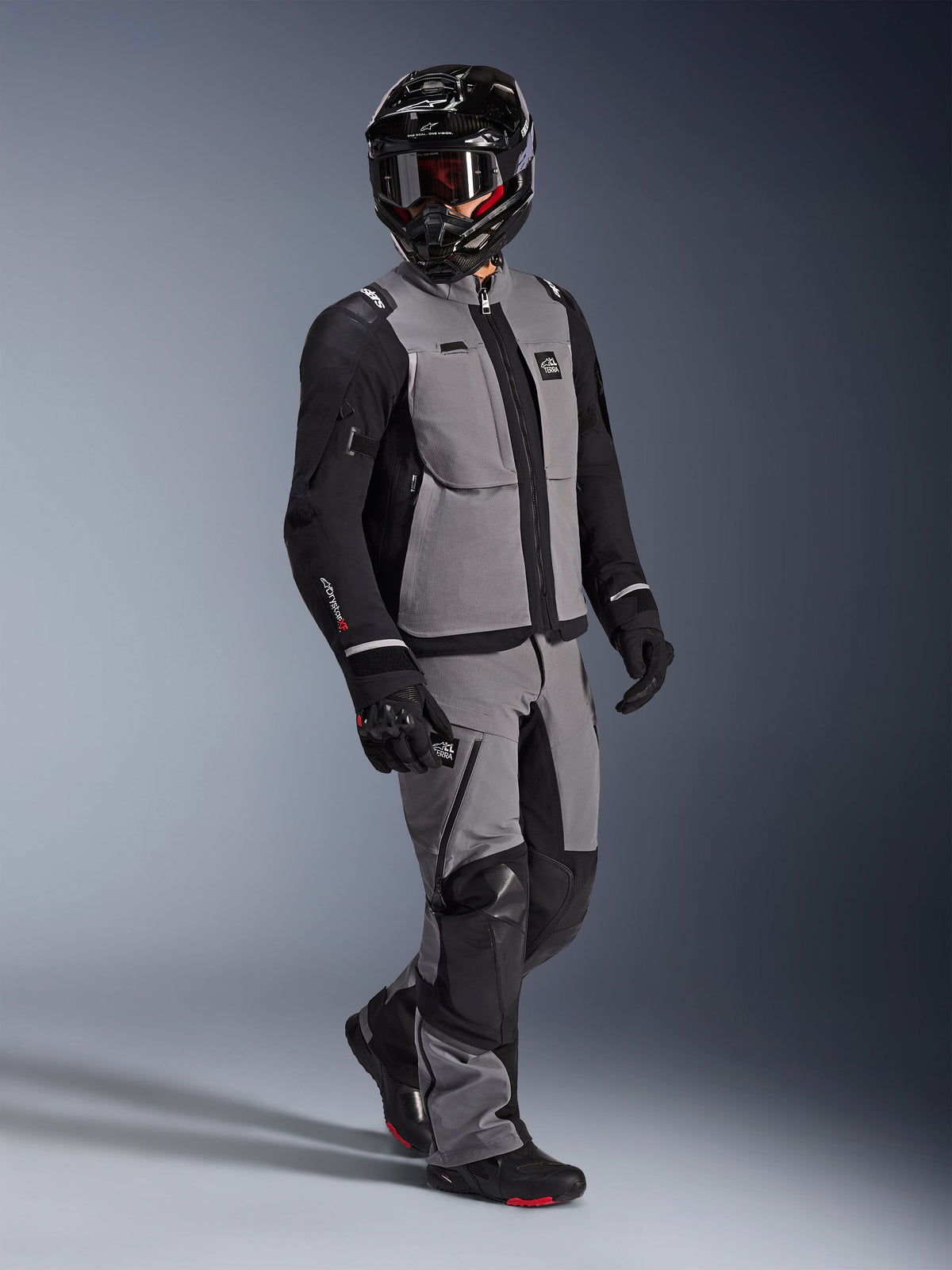 Adventure rider wearing the Alpinestars Andes Pro Drystar® XF Jacket in Dark Gray and Black, matching gray and black adventure pants, black full-face helmet with goggles, and black motorcycle gloves, studio shot for professional long-distance touring gear.