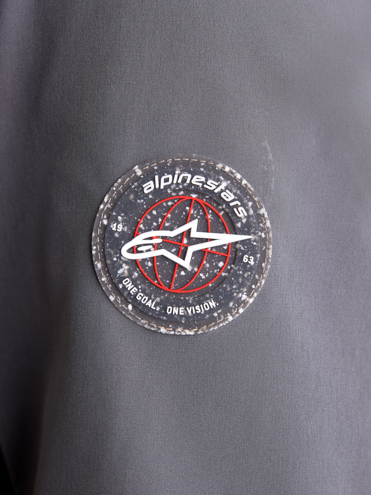 Alpinestars Therma-Tech Waterproof Jacket, close-up view of the circular brand logo patch on the dark gray and black textile sleeve, showcasing the A-star emblem and signature branding