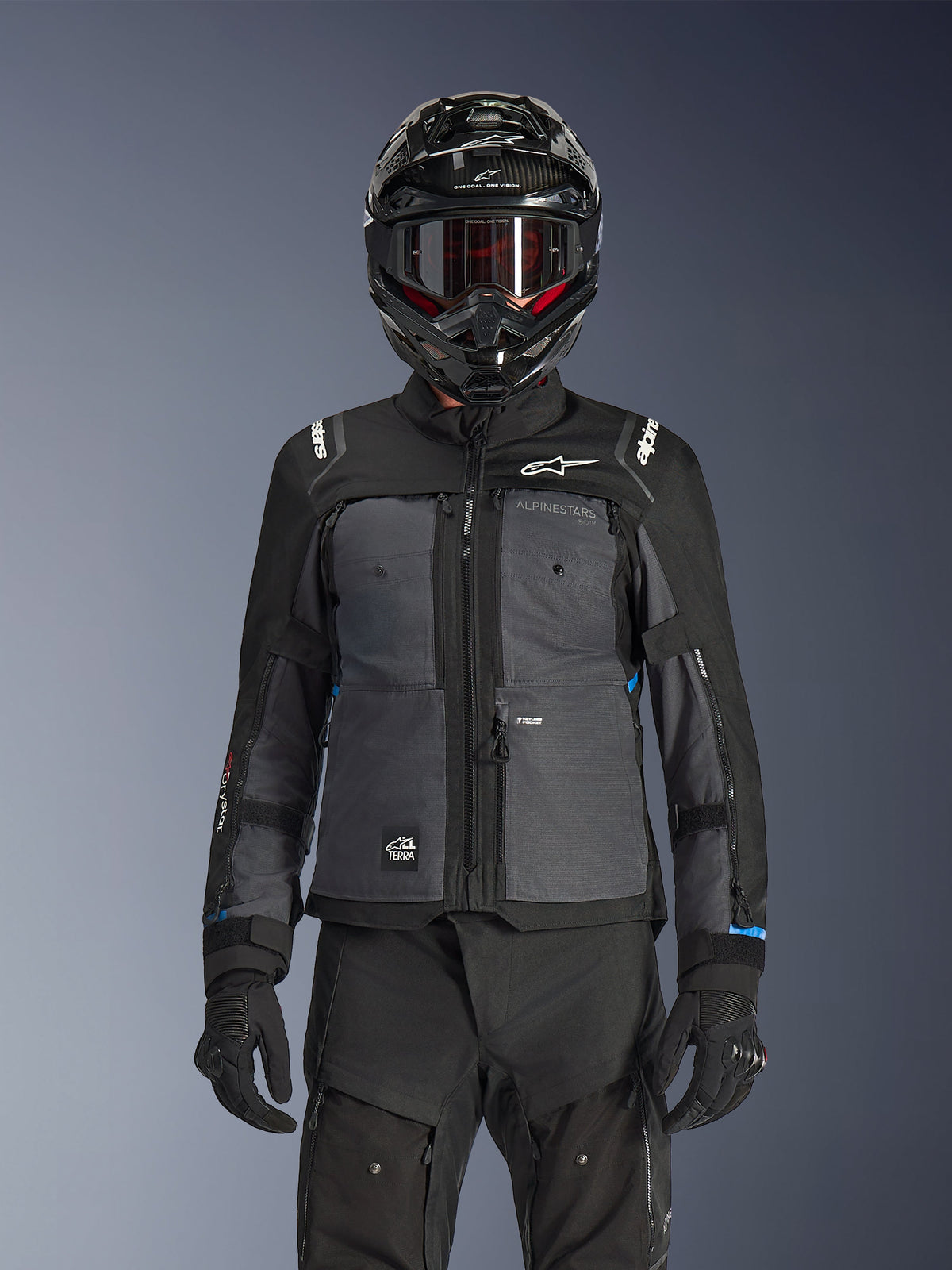 Kurtka Alpinestars Cusco Drystar®, czarna i ciemnoszara, motocyklowa kurtka adventure touring noszona z pasującymi czarnymi spodniami technicznymi i kaskiem dual-sport, dwukolorowy design z panelami ripstop i brandingiem Alpinestars