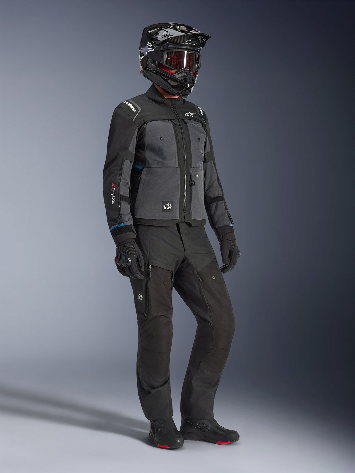 Model w kurtce Alpinestars Cusco Drystar® w kolorze czarnym i ciemnoszarym, w pełnym stroju motocyklowym z czarnym kaskiem, technicznymi spodniami, rękawicami i butami; konstrukcja ripstop i softshell do jazdy szosowej i adventure touring
