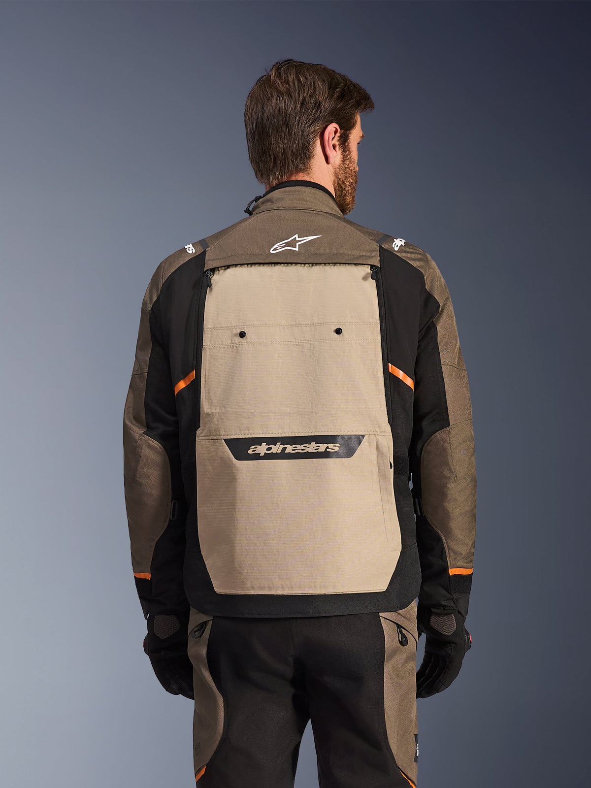 Kurtka Alpinestars Cusco Drystar®, Walnut Aluminum Black, widok z tyłu, duży beżowy panel na plecach z czarnym logo, pomarańczowe akcenty, noszona z pasującymi spodniami i rękawicami, zaprojektowana do jazdy adventure touring