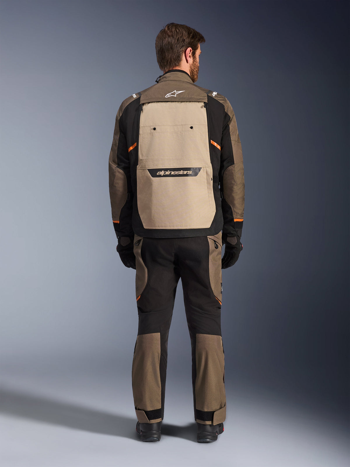 Kurtka Alpinestars Cusco Drystar®, widok od tyłu, kolor Walnut Aluminum Black, tekstylna odzież motocyklowa typu adventure touring, duży beżowy panel wentylacyjny na plecach z czarnym logotypem, pomarańczowe akcenty, noszona z pasującymi spodniami i rękawicami