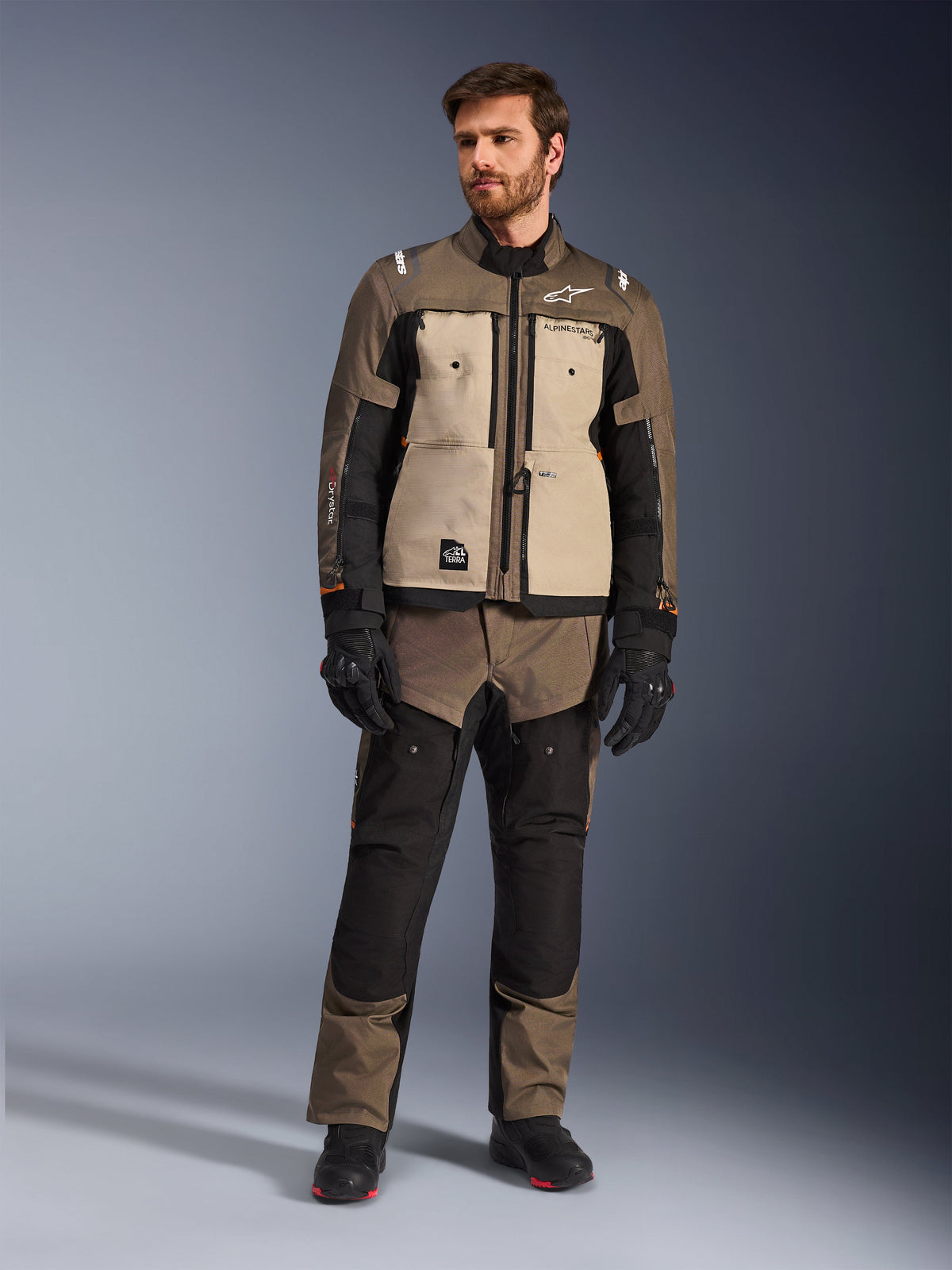 Kurtka Alpinestars Cusco Drystar® w kolorze Walnut Aluminum Black, noszona przez motocyklistę z pasującymi spodniami adventure touring, czarnymi rękawicami i butami, wyposażona w beżowe panele na klatce piersiowej, czarne rękawy z subtelnymi pomarańczowymi akcentami i funkcjonalne zamki wentylacyjne do drogowej jazdy motocyklowej.
