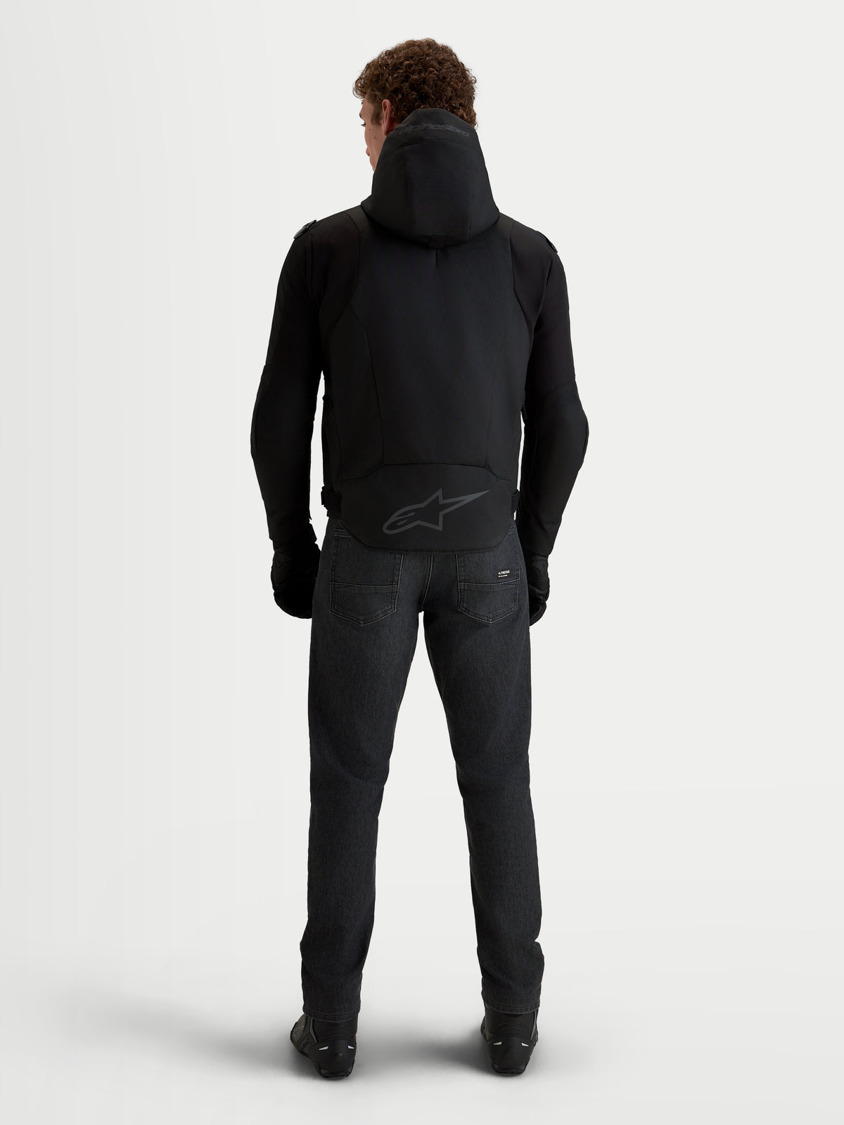 Alpinestars Zaca V2 Waterproof, męska czarna kurtka motocyklowa, widok z tyłu, z zintegrowanym kapturem, przedłużonym tyłem z tonalnym logo oraz ochronną konstrukcją do jazdy