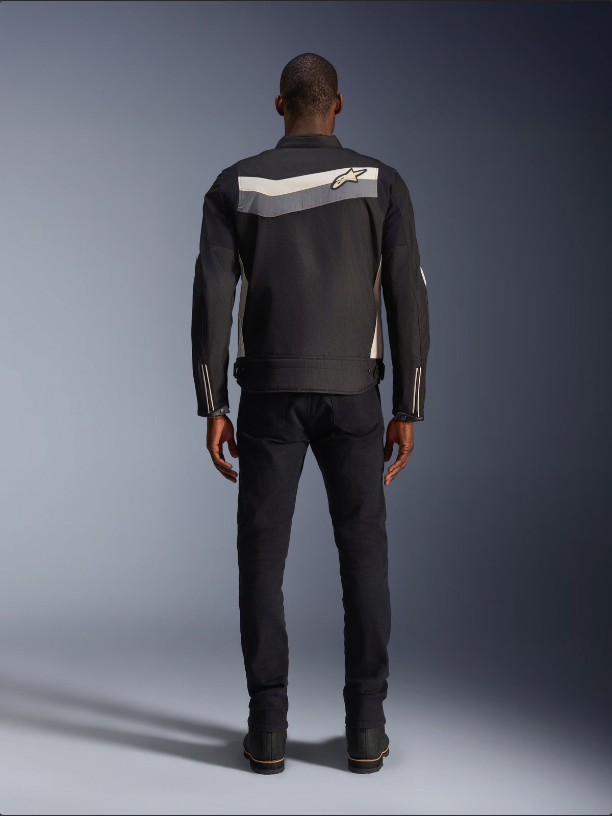 Alpinestars T-Dyno WR Jacket, textile motorcycle jacket, Black Dark Gray and Ecru, back view showing horizontal stripe across shoulders with small star logo, worn by model with black pants and boots, vintage-inspired road riding gear