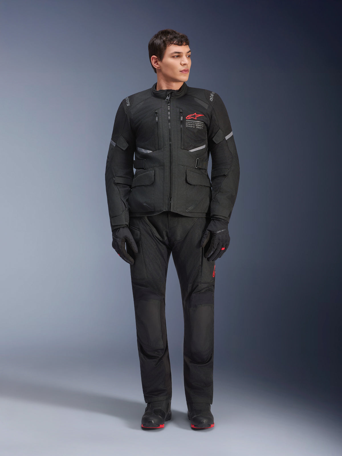 Alpinestars Andes Air Drystar® Pants, motocyklowe spodnie turystyczne, czarne, z siatkowymi panelami wentylacyjnymi i czerwonym logo na nogawce, noszone jako część pełnego stroju z pasującą kurtką i rękawicami, profesjonalna odzież turystyczna adventure