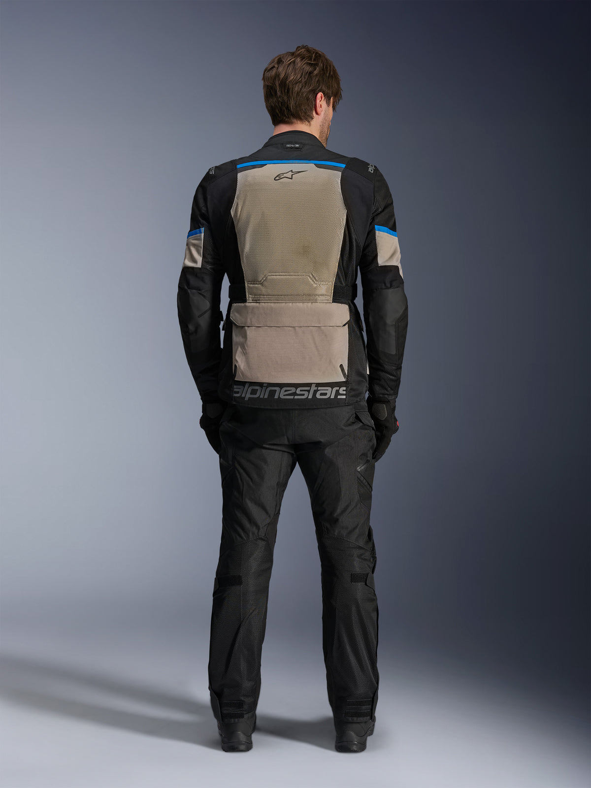 Kurtka Alpinestars Andes Air Drystar®, Black Laurel Gray Bright Blue, widok z tyłu ukazujący obszerny panel wentylacyjny z siatki, duża kieszeń w dolnej części pleców z logo Alpinestars, techniczna motocyklowa kurtka turystyczna noszona z pasującymi spodniami.