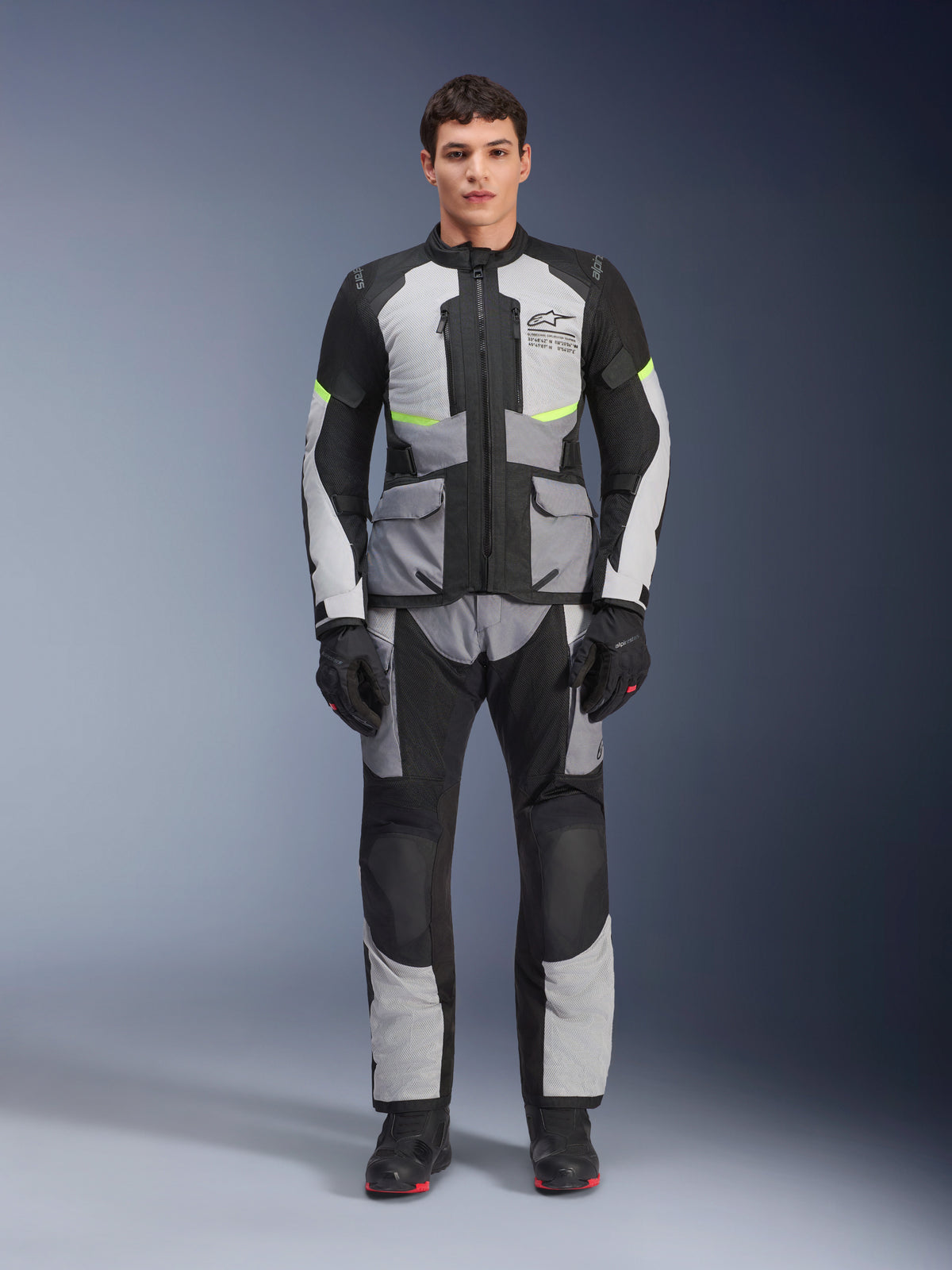 Alpinestars Andes Air Drystar® Pants, turystyczne spodnie motocyklowe adventure, szare i czarne z neonowożółtymi akcentami, widok na całą sylwetkę modela w pasującej kurtce i rękawicach, tekstylna konstrukcja z siatkowymi panelami wentylacyjnymi