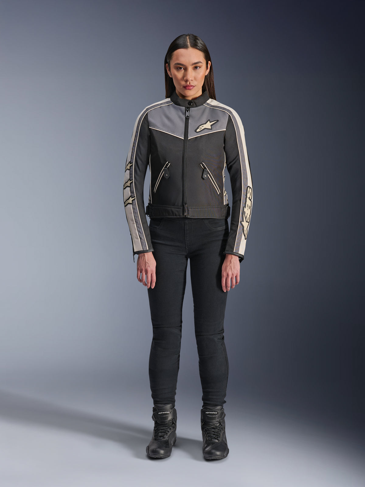 Kobieta ubrana w kurtkę Alpinestars Stella T-Dyno WR, czarny, ciemnoszary i ecru, widok z przodu, tekstylna kurtka motocyklowa o designie inspirowanym stylem vintage, z logo na klatce piersiowej i rękawach, noszona z czarnymi spodniami i butami