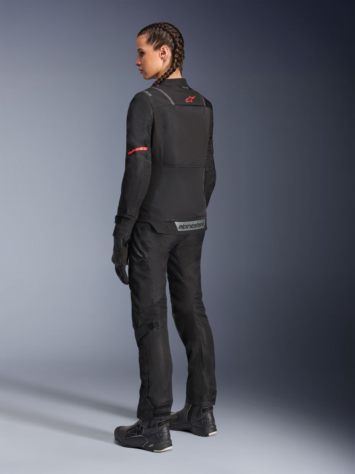 Kurtka Alpinestars Stella ST-2 Air, damska kurtka motocyklowa, czarna z czerwonymi akcentami na rękawach i górnej części pleców, widok z tyłu na modelce ubranej w pasujące czarne spodnie motocyklowe i buty, z odblaskowym brandingiem Alpinestars i nowoczesną konstrukcją tekstylną.