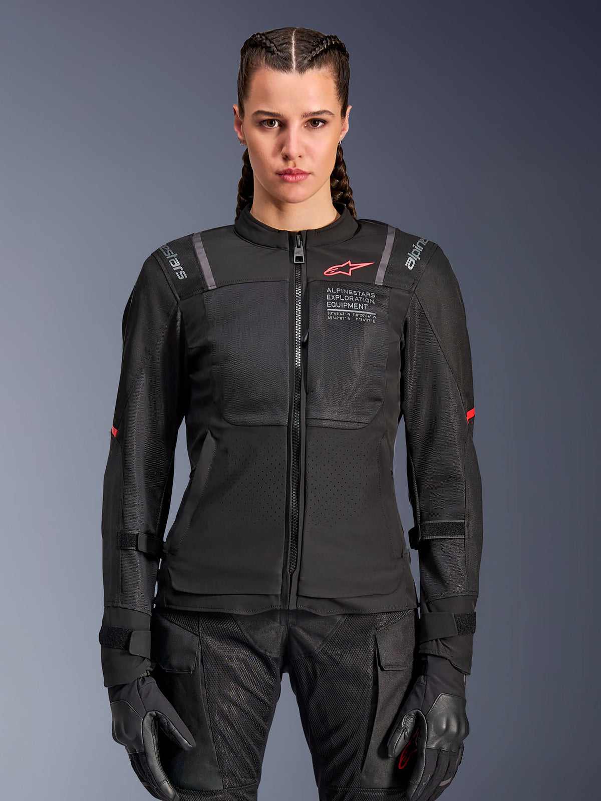 Alpinestars Woman Stella ST-2 Air Jacket, damska kurtka motocyklowa, czarna, widok z przodu na modelce, z panelami z siatki, czerwonym logo na klatce piersiowej i brandingiem Alpinestars Exploration Equipment, noszona z czarnymi rękawicami i spodniami motocyklowymi