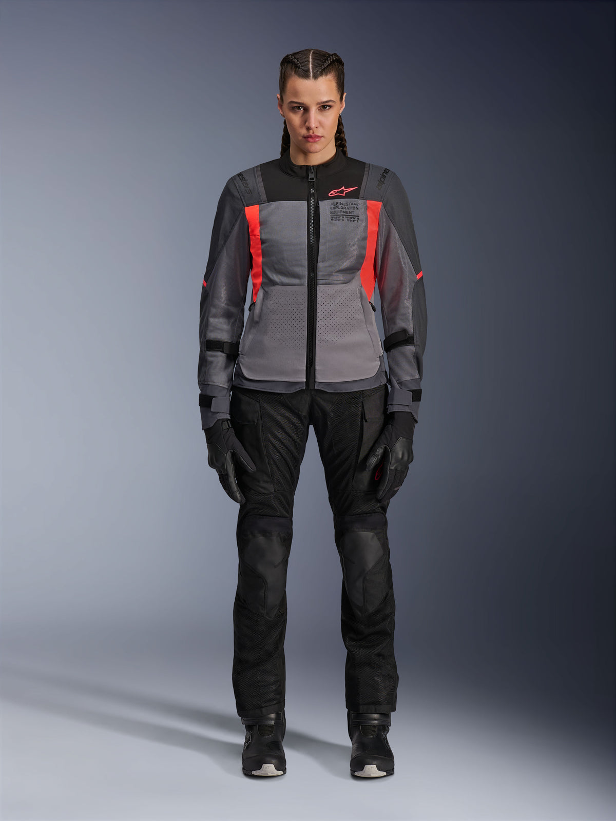 Kobieta w kurtce Alpinestars Stella ST-2 Air w kolorach Deep Gray, Dark Gray i Fluo Coral, w zestawie z czarnymi spodniami motocyklowymi i rękawicami, widok z przodu, nowoczesna siatkowa odzież adventure touring dla kobiet