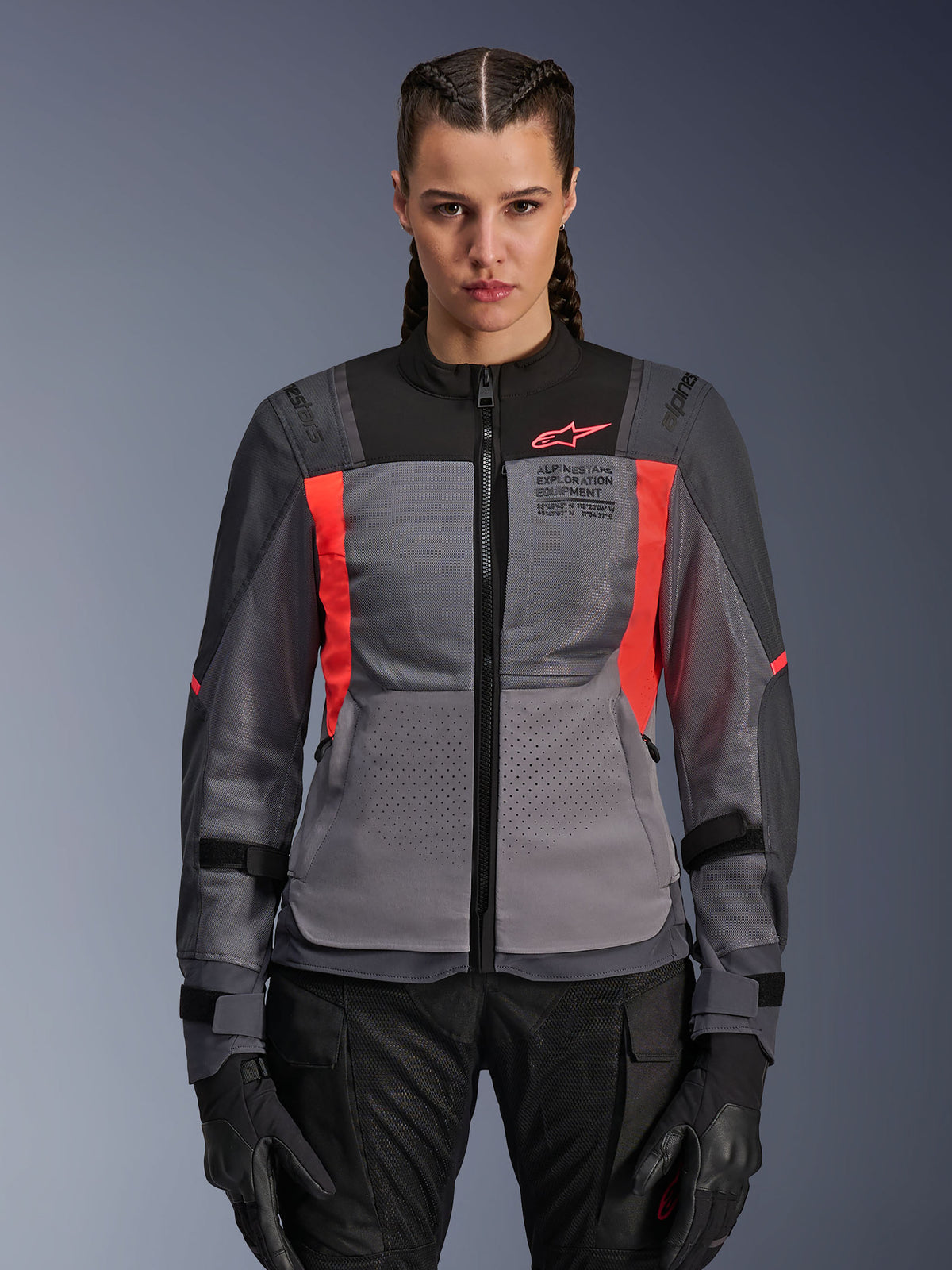 Alpinestars Stella ST-2 Air Jacket, damska kurtka motocyklowa, ciemnoszara i koralowa Fluo Coral, modelka w wentylowanej kurtce tekstylnej z panelami z siatki, jaskrawokoralowe akcenty i branding na klatce piersiowej, nowoczesny styl adventure