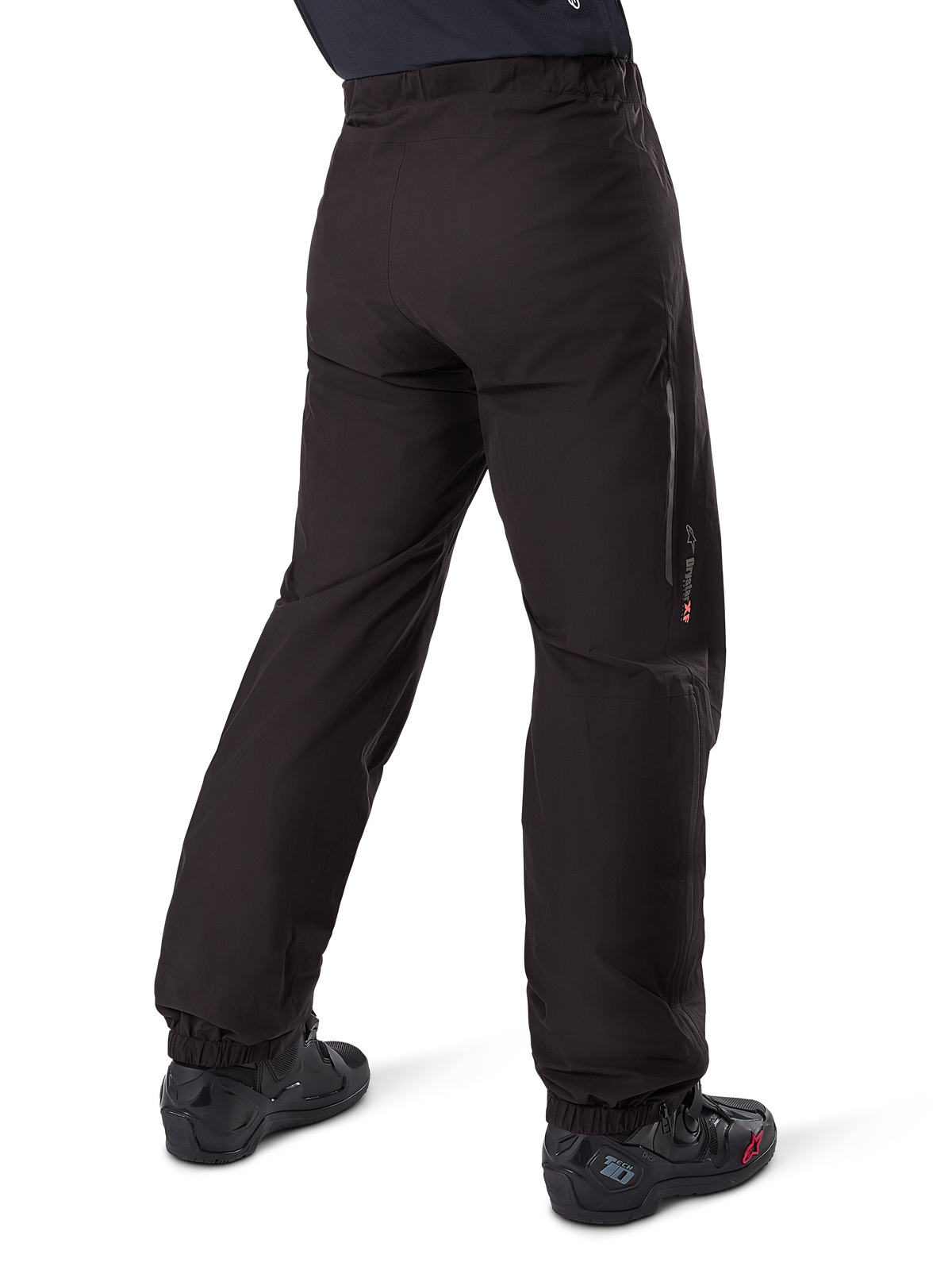Podpinka Alpinestars Amt-8 Stretch Drystar® XF, czarna, widok z tyłu przedstawiający wodoodporną warstwę założoną na czarne buty motocyklowe, logo Drystar XF na dole nogawki, elastyczne mankiety, lekki i rozciągliwy materiał do turystyki przygodowej.