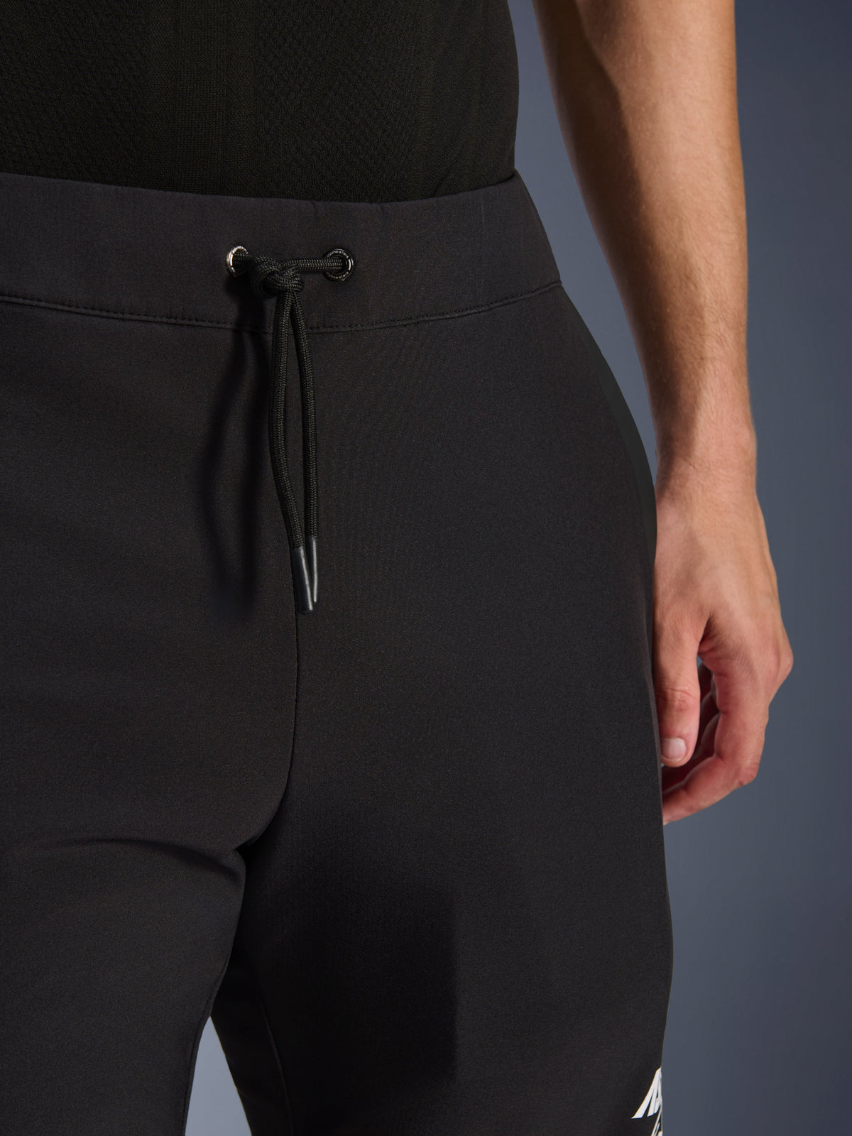 Alpinestars Aeroshell Pants, czarne motocyklowe spodnie softshellowe, zbliżenie na elastyczny pas i zapięcie na sznurek, nowoczesny minimalistyczny design, wytrzymała konstrukcja tekstylna do casualowej jazdy turystycznej