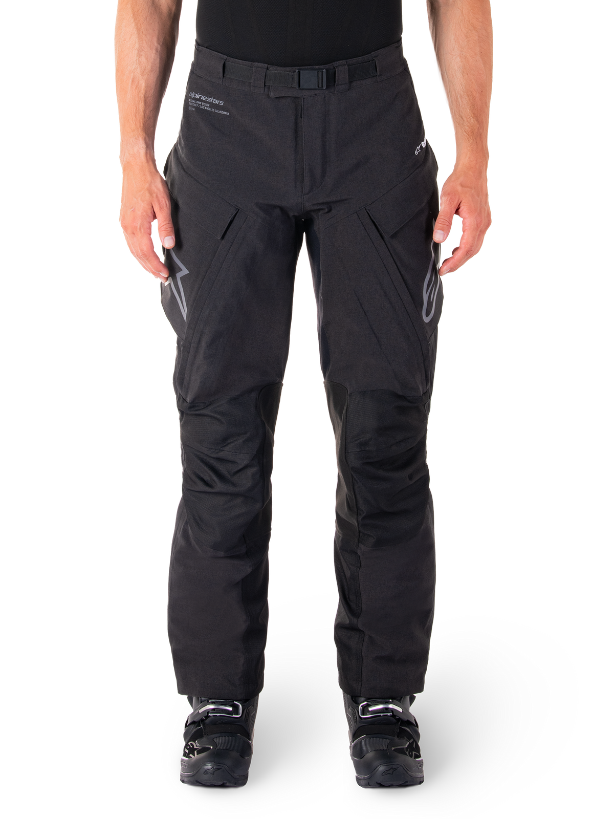 Alpinestars Hyde XT Drystar Pants, czarne spodnie motocyklowe adventure touring, noszone przez motocyklistę w czarnych butach, szare logo na udach, zintegrowany pas, wzmocnione panele na kolanach, wodoodporna konstrukcja tekstylna