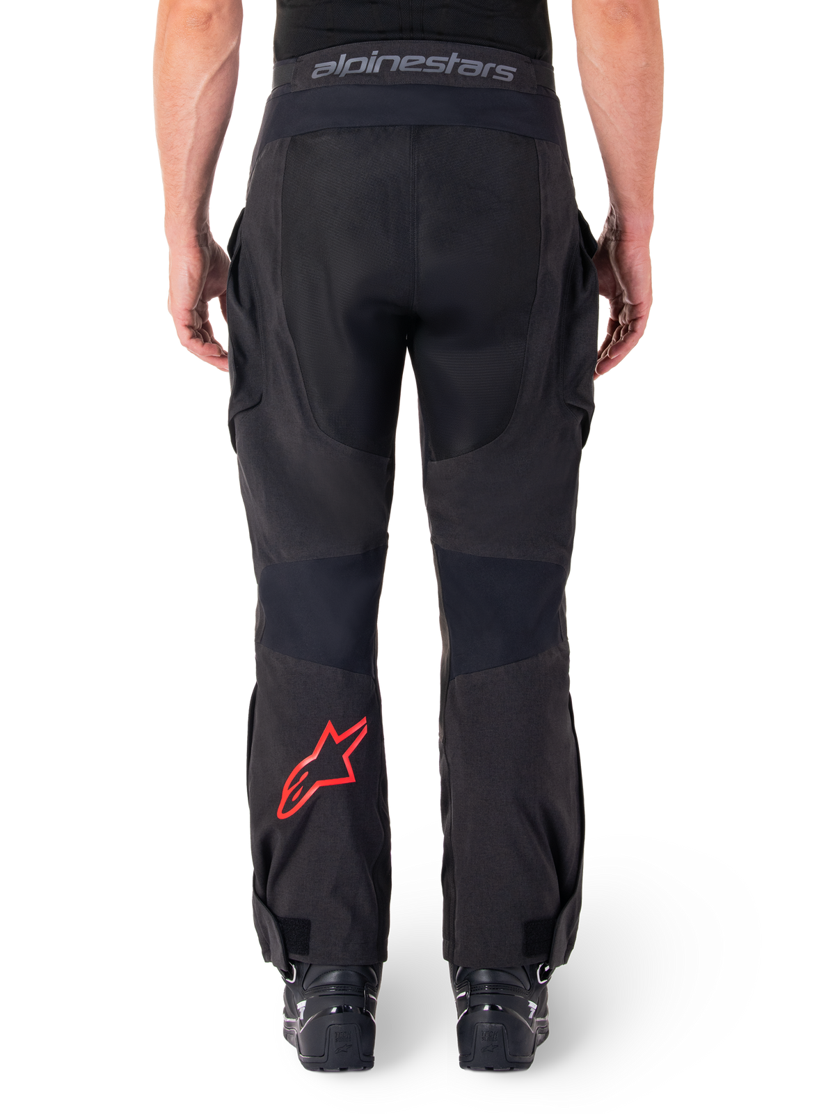 Spodnie Alpinestars Hyde XT Drystar®, motocyklowe spodnie adventure, czarne z czerwonym logo gwiazdy na dole nogawki, widok z tyłu, konstrukcja enduro zakładana na buty, trwałe panele tekstylne i pas z logo.