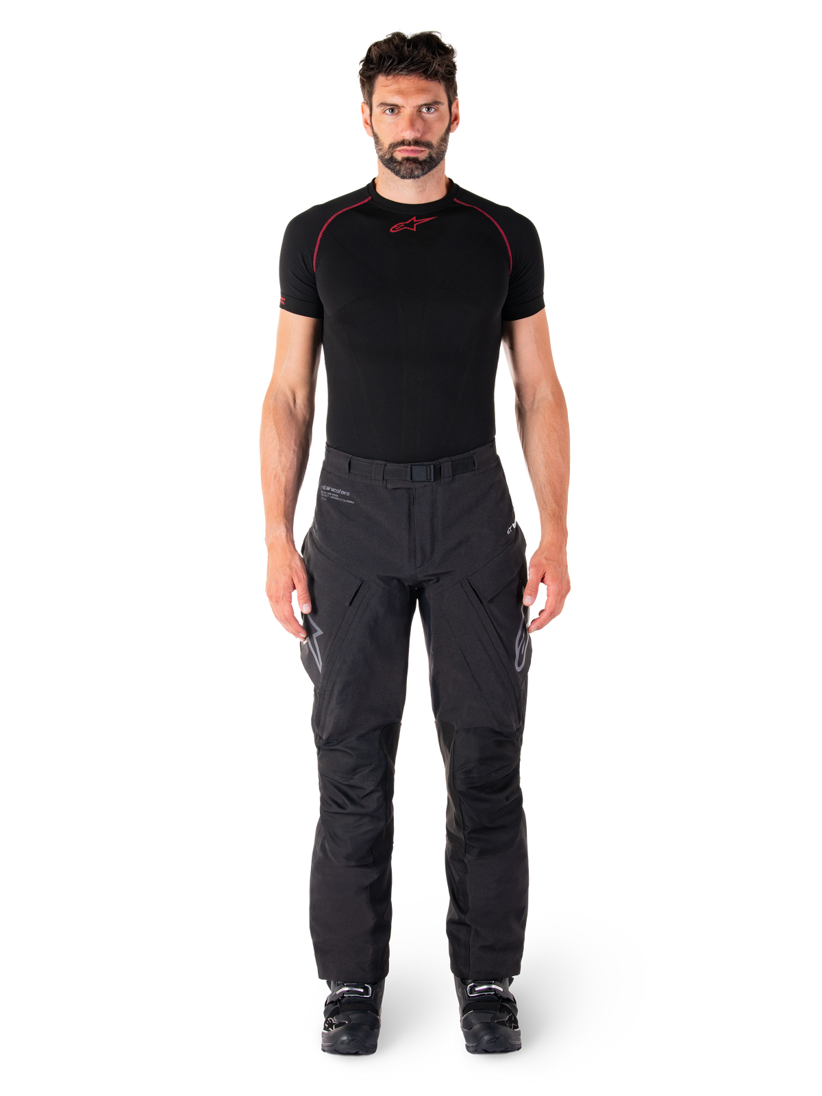 Spodnie Alpinestars Hyde XT Drystar®, motocyklowe spodnie adventure touring, czarne, prezentowane przez modela w czarnej warstwie bazowej z krótkim rękawem i czarnych butach, wyposażone w techniczny materiał stretch, wzmocnione panele na kolanach oraz ergonomiczne kieszenie cargo.