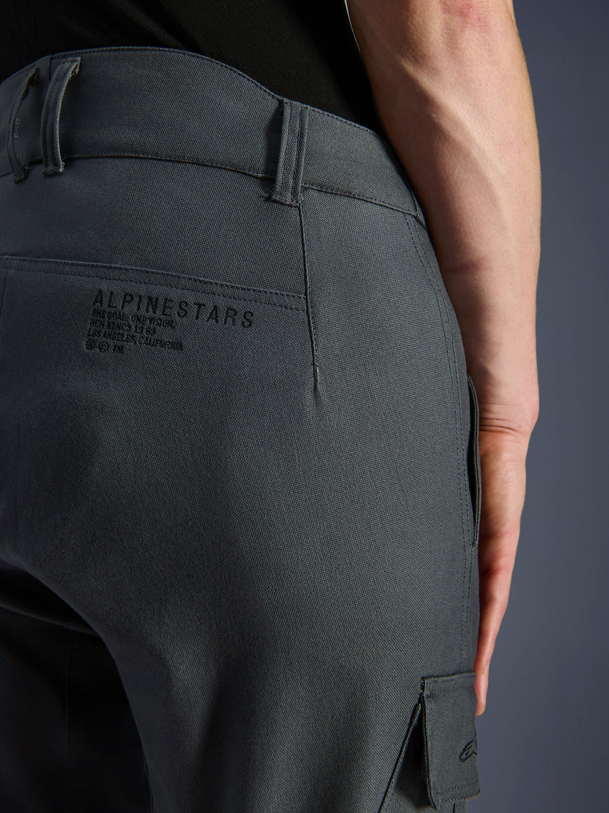 Alpinestars Borrego Drystar® Pants, spodnie motocyklowe, kolor szary antracytowy, zbliżenie na tylną część biodra z logo i sloganem Alpinestars, wytrzymały materiał o wyglądzie woskowanego płótna, odzież do jazdy adventure
