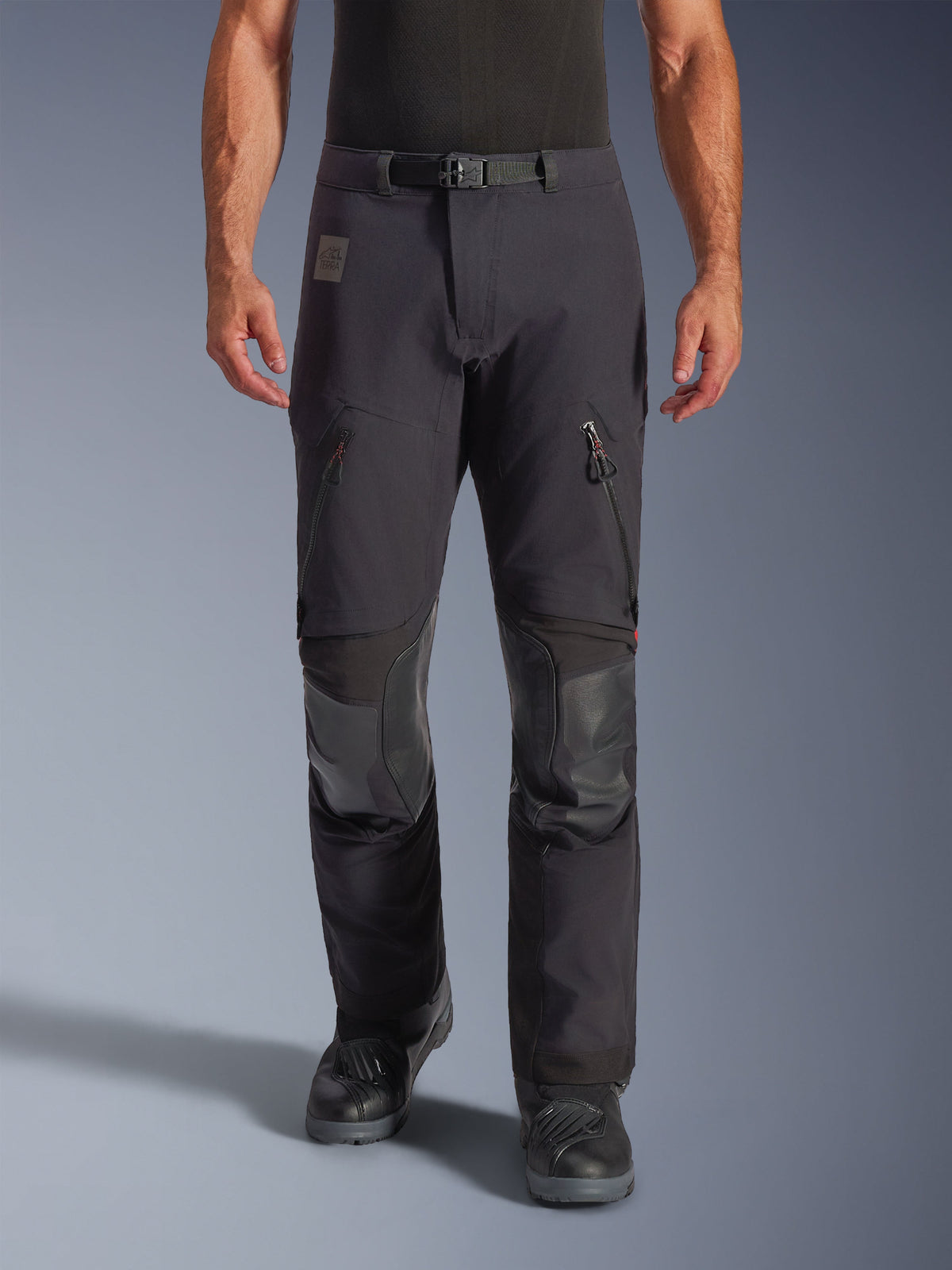 Alpinestars Halo Pro Drystar® XF Laminated Pants w kolorze Black Dark Shadow, motocyklowe spodnie adventure, widok z przodu na modelu, magnetyczna klamra w pasie, otwory wentylacyjne na udach zapinane na zamek, wzmocnione skórzane łaty na kolanach, czarne buty motocyklowe