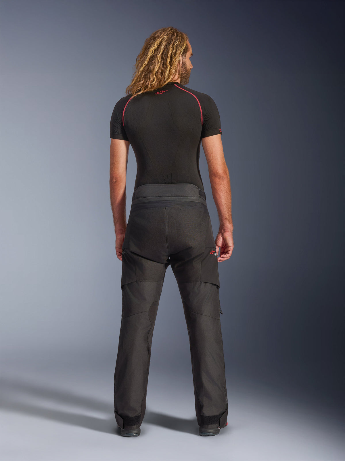 Widok z tyłu modelu w spodniach Alpinestars Andes V4 Drystar® - Short, czarne motocyklowe spodnie adventure, zestawione z czarną warstwą bazową z czerwonymi szwami, prezentujące wytrzymałą konstrukcję tekstylną i ergonomiczne dopasowanie.