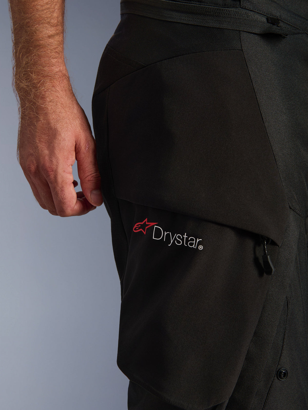 Alpinestars Andes V4 Drystar® Pants, detal czarnej kieszeni cargo z białym logo Drystar i czerwoną gwiazdą, prezentujący wytrzymałą konstrukcję tekstylną oraz elementy zamka błyskawicznego.