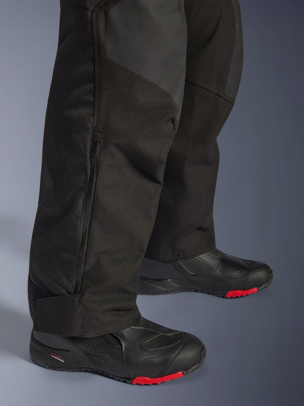 Alpinestars Andes V4 Drystar® Pants - Short, czarne, zbliżenie na detale dolnej części nogawki przedstawiające konstrukcję tekstylną, pionowy zamek wentylacyjny oraz regulowane mankiety na kostkach, noszone z czarnymi butami motocyklowymi