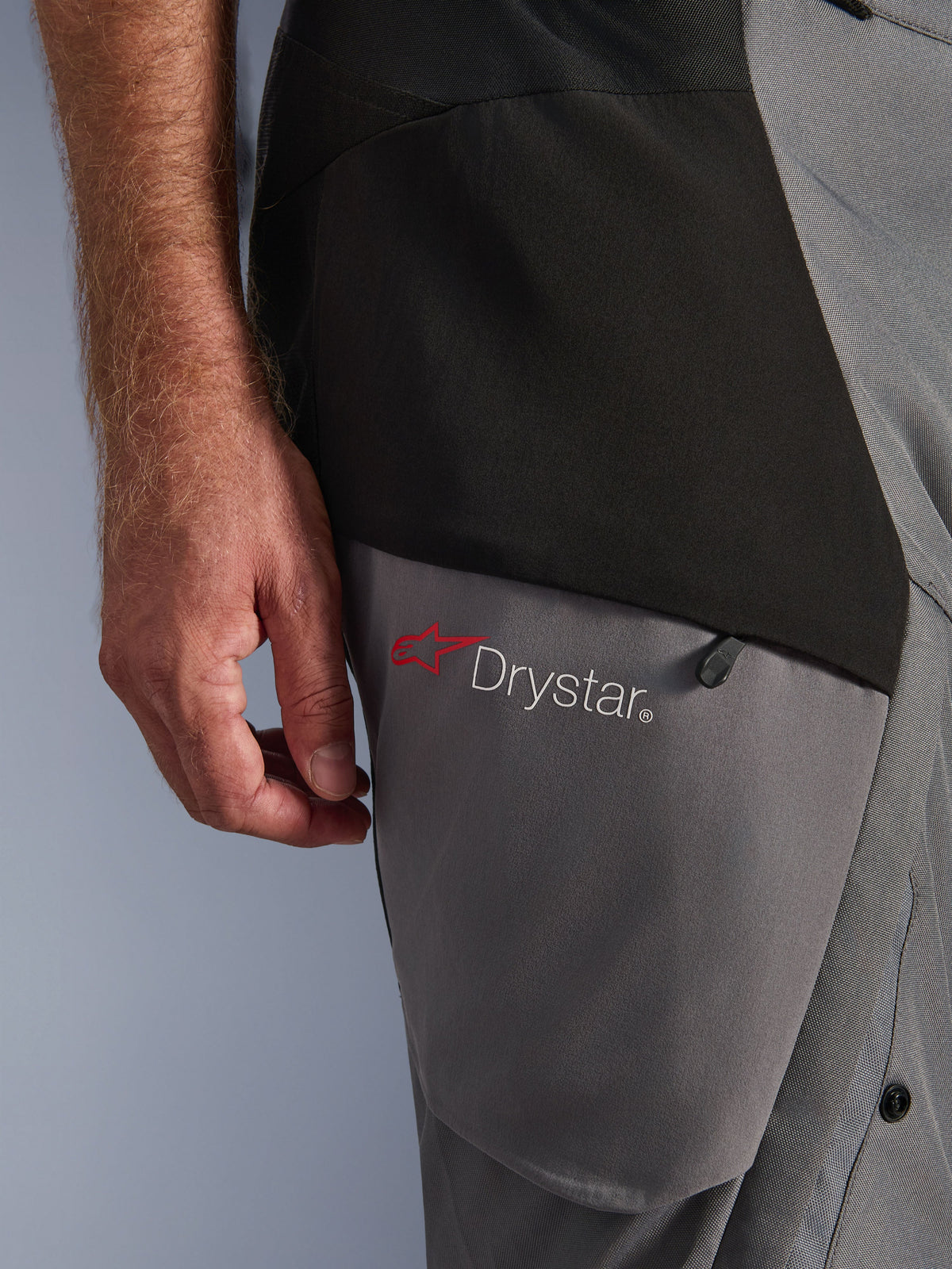 Alpinestars Andes V4 Drystar® Pants, czarno-ciemnoszare, zbliżenie na detal na udzie z czerwonym logo gwiazdy i brandingiem Drystar®, wytrzymała konstrukcja tekstylna z kieszenią na zamek, odzież motocyklowa adventure