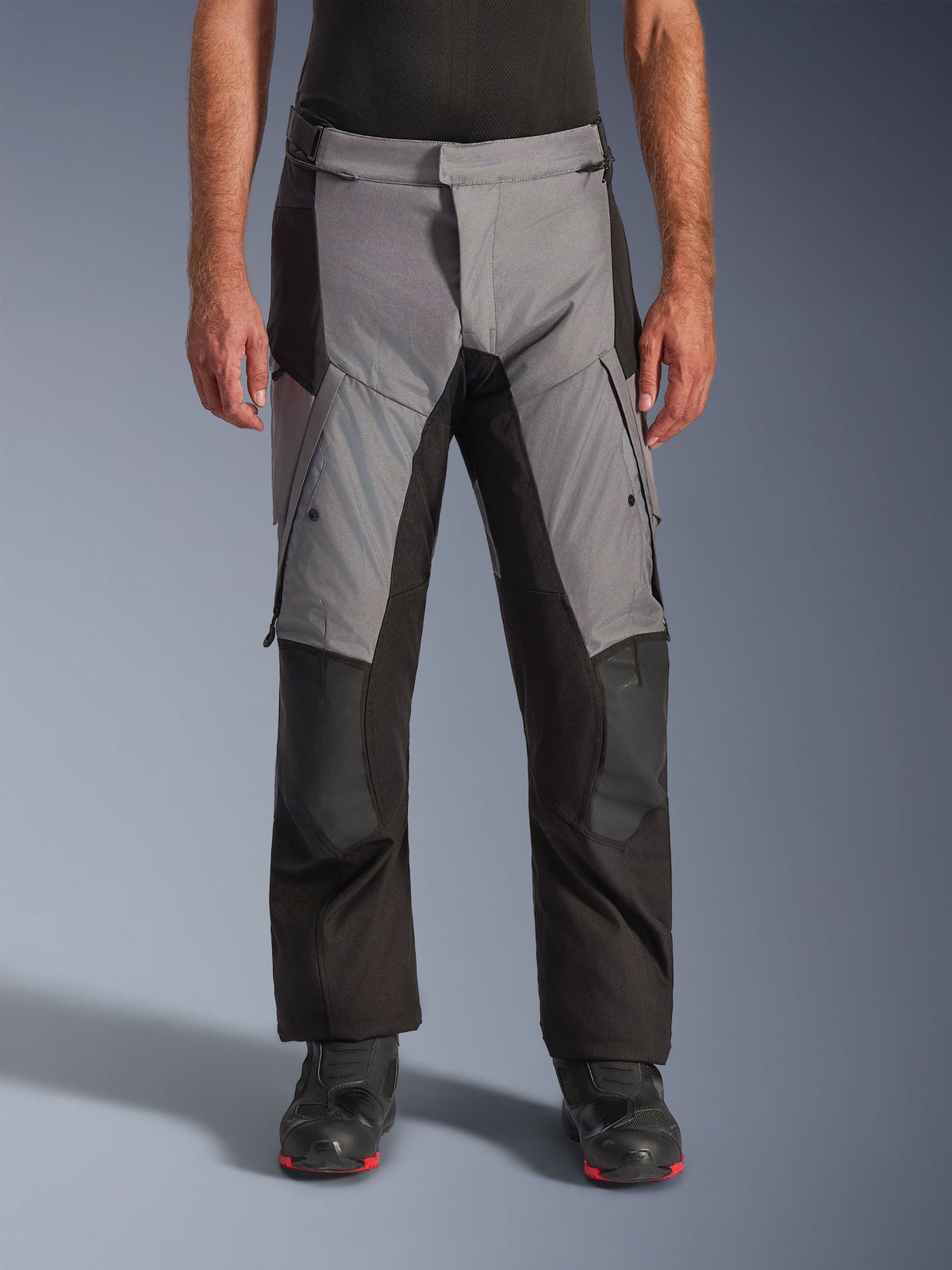 Alpinestars Andes V4 Drystar® Pants, motocyklowe spodnie turystyczne adventure, szaro-czarne, widok z przodu na modelu w czarnych butach motocyklowych, wzmocnione panele na kolanach i kieszenie cargo na udach, wodoodporna i oddychająca konstrukcja tekstylna do jazdy w każdą pogodę