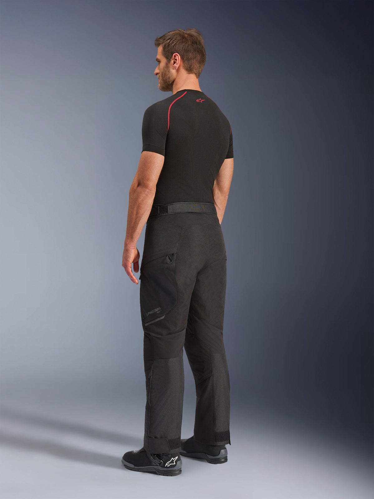 Alpinestars Cusco Drystar® Pants, Motorcycle Adventure Pants, Black, worn by model from a side and rear view, paired with a black base layer and black riding boots, technical textile construction with zippered pockets and articulated knees