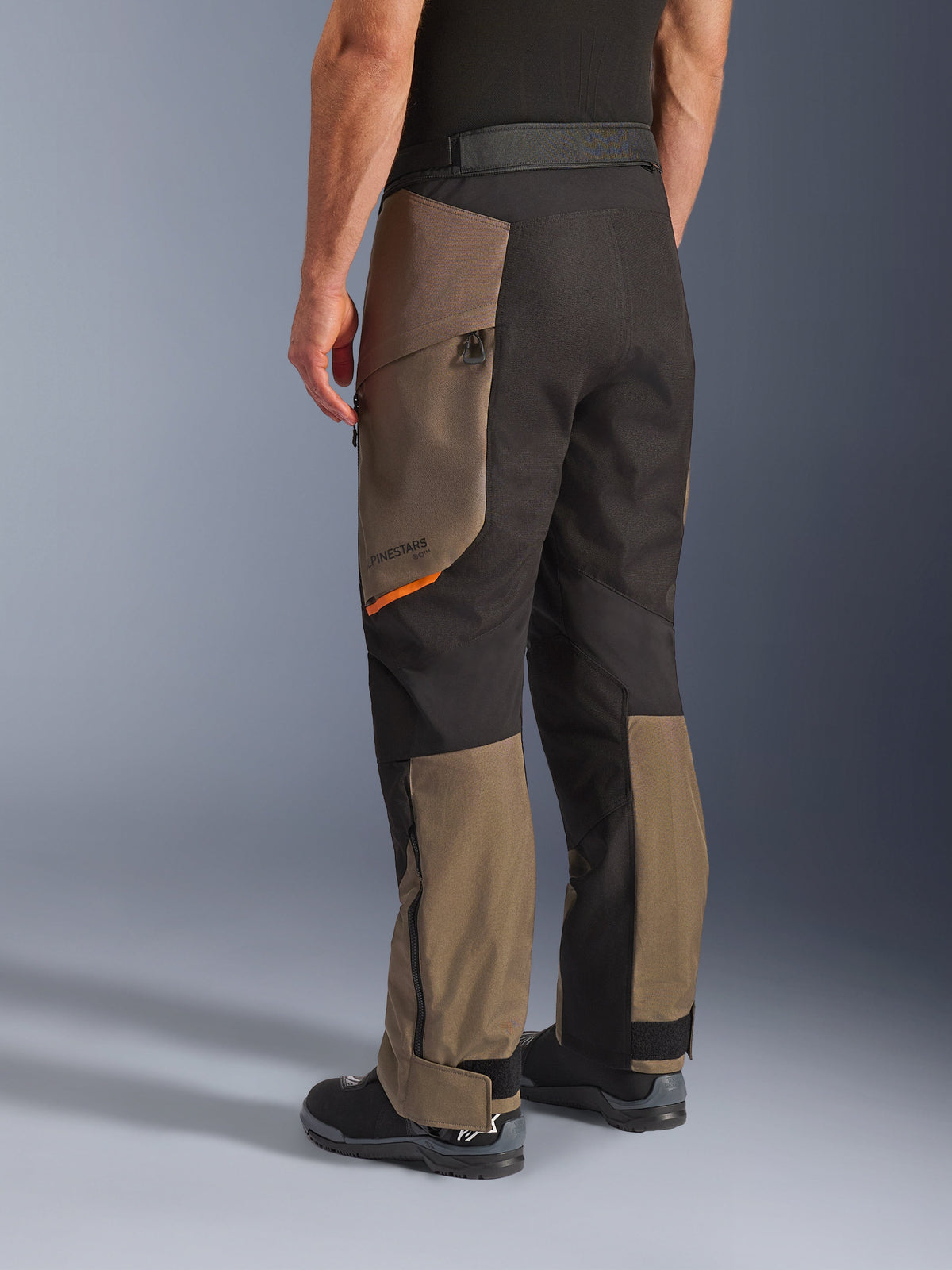 Alpinestars Cusco Drystar® Pants, Adventure Motorcycle Pants, Walnut Black with small orange accent, rear three-quarter view showing textile construction and walnut panels, worn with black motorcycle boots.