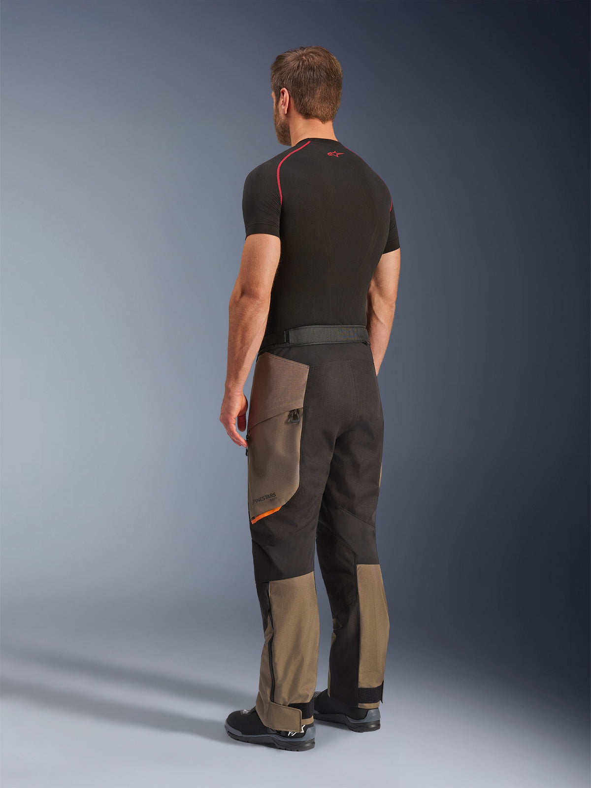 Alpinestars Cusco Drystar® Pants, Adventure Motorcycle Pants, Walnut Black, rear three-quarter view worn with a black base layer and boots, featuring reinforced textile panels, zippered cargo pockets on the thighs, and an ergonomic touring fit.