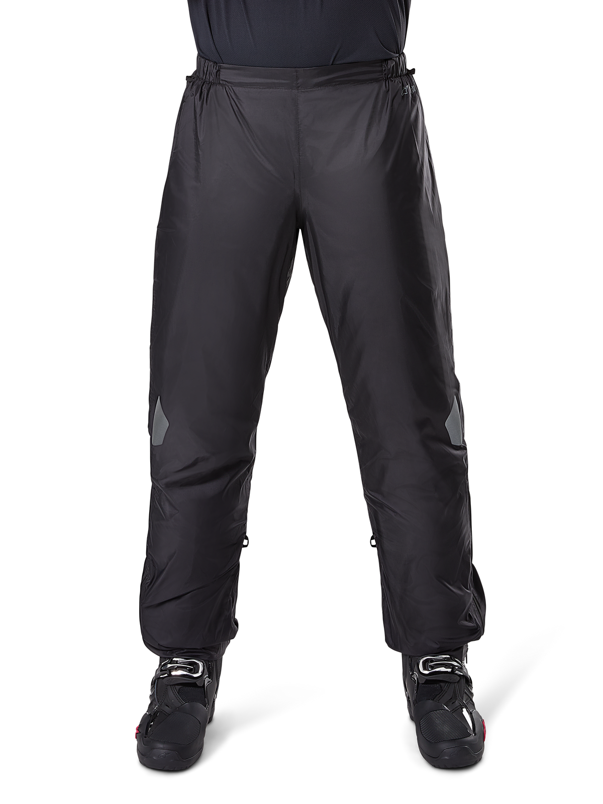 Alpinestars Bogota Pro Drystar 3 Seasons Pants, wodoodporne spodnie motocyklowe, czarne, lekka tkanina techniczna z odblaskowymi naszywkami na kolanach, noszone jako spodnie wierzchnie z czarnymi butami motocyklowymi, zaprojektowane dla ochrony przed warunkami pogodowymi w turystyce adventure