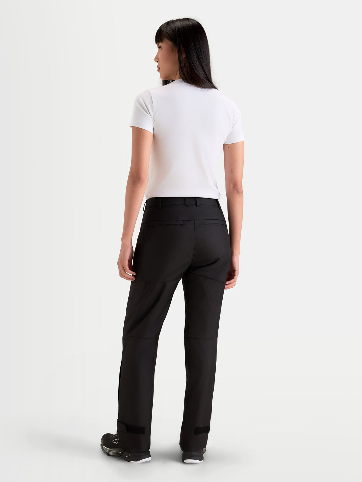 Alpinestars Stella C-1 Waterproof Pants, women's urban motorcycle pants in black, rear profile view on a model wearing a white t-shirt and riding shoes, featuring a durable 450D polyfabric construction and weather protection.