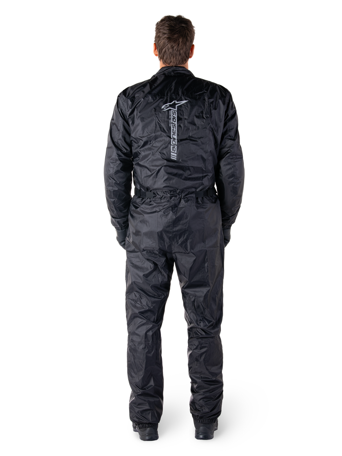 Alpinestars Hurricane Rain V2 Suit, czarny jednoczęściowy wodoodporny kombinezon motocyklowy, widok z tyłu z dużym pionowym napisem i logo Alpinestars, lekki marszczony materiał z elastycznym pasem i mankietami, zaprojektowany do ochrony podczas jazdy w deszczu.