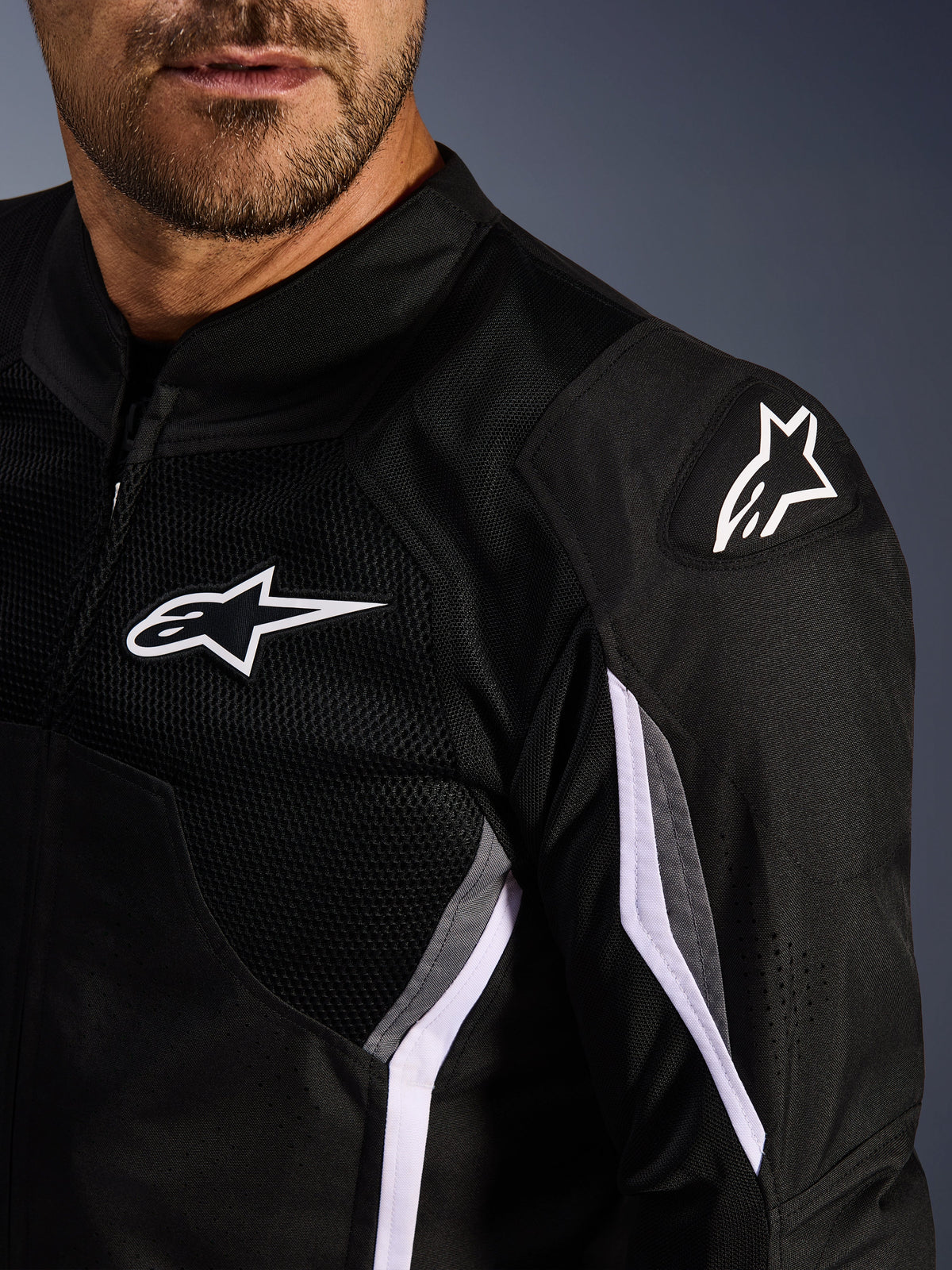 Alpinestars AST V3 Air Jacket, tekstylna kurtka motocyklowa, czarna z ciemnoszarymi i białymi detalami, zbliżenie na panele z siatki, białe logo Alpinestars na klatce piersiowej i ramieniu oraz zewnętrzne ślizgacze ramion DFS GP Lite Evo