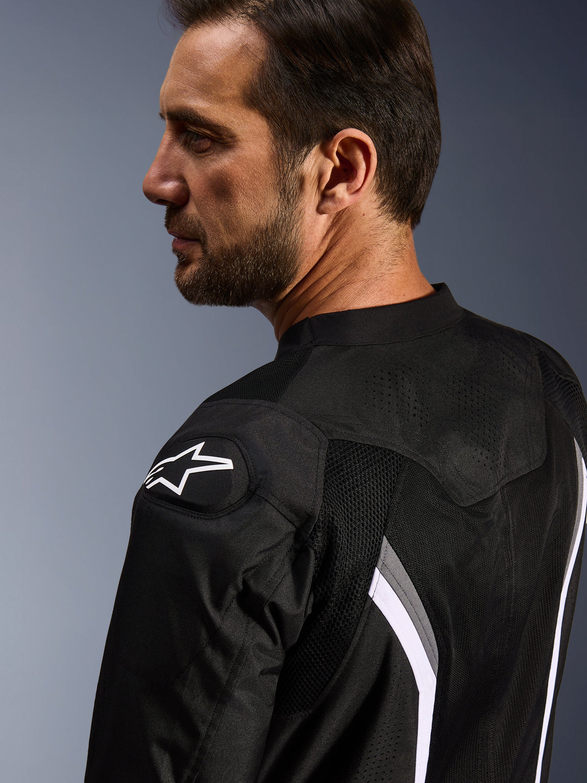 Alpinestars AST V3 Air Jacket, motocyklowa kurtka letnia, czarna, ciemnoszara i biała, widok z bliska od tyłu pokazujący białe logo gwiazdy na ramieniu oraz laserowo perforowane panele z siatki zapewniające wentylację.