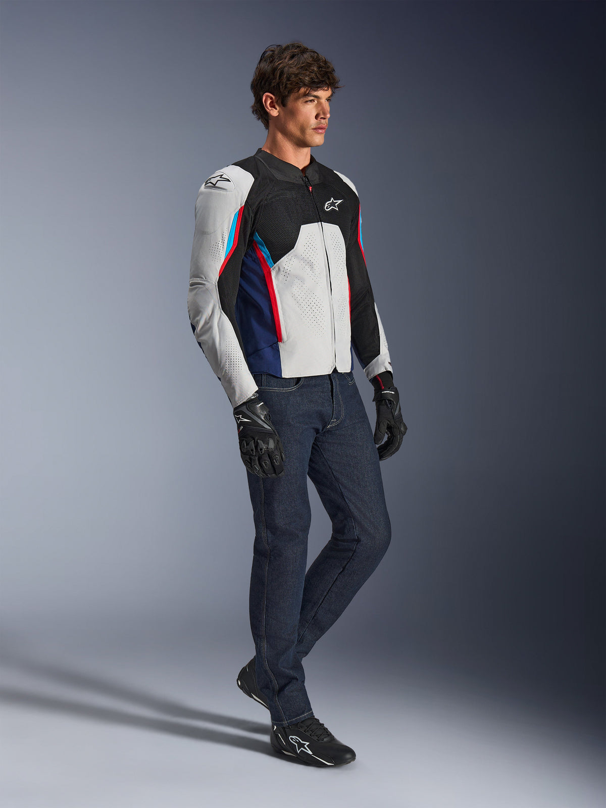 Alpinestars AST V3 Air Jacket, kurtka motocyklowa, srebrna, ciemnoniebieska i jaskrawoczerwona, noszona z ciemnymi jeansami i czarnymi rękawicami, z wentylowanymi panelami z siatki i sportowym krojem na ciepłe dni