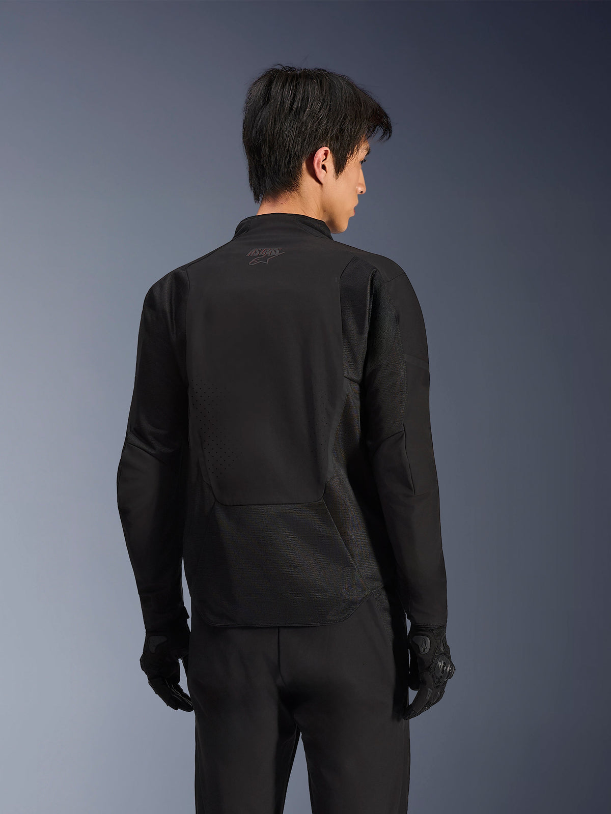 Kurtka Alpinestars Aeroshell Airflow, Black Anthracite, widok z tyłu sportowej kurtki motocyklowej z laserowo perforowanymi strefami wentylacyjnymi i panelami z siatki 2D, wydłużony tył dla lepszej osłony, noszona z czarnymi rękawicami motocyklowymi