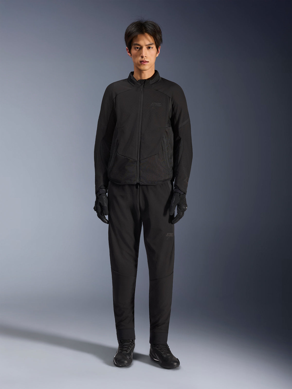 Alpinestars Aeroshell Airflow Jacket, Black motorcycle jacket, worn by model with matching black pants and gloves, featuring laser-perforated chest and side mesh panels, sport-cut fit for warm-weather performance