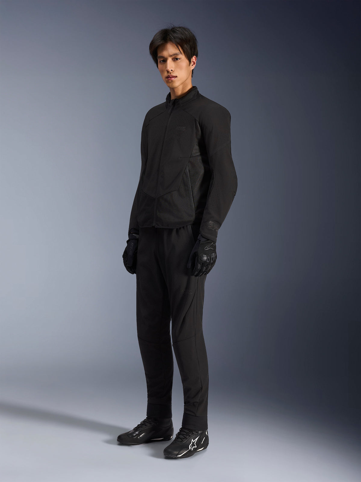 Alpinestars Aeroshell Airflow Jacket, Black Anthracite motorcycle jacket, featuring laser-perforated ventilation and mesh panels for airflow, worn by a male model with matching black riding pants, gloves, and black boots with white logos, sport-cut design for road performance