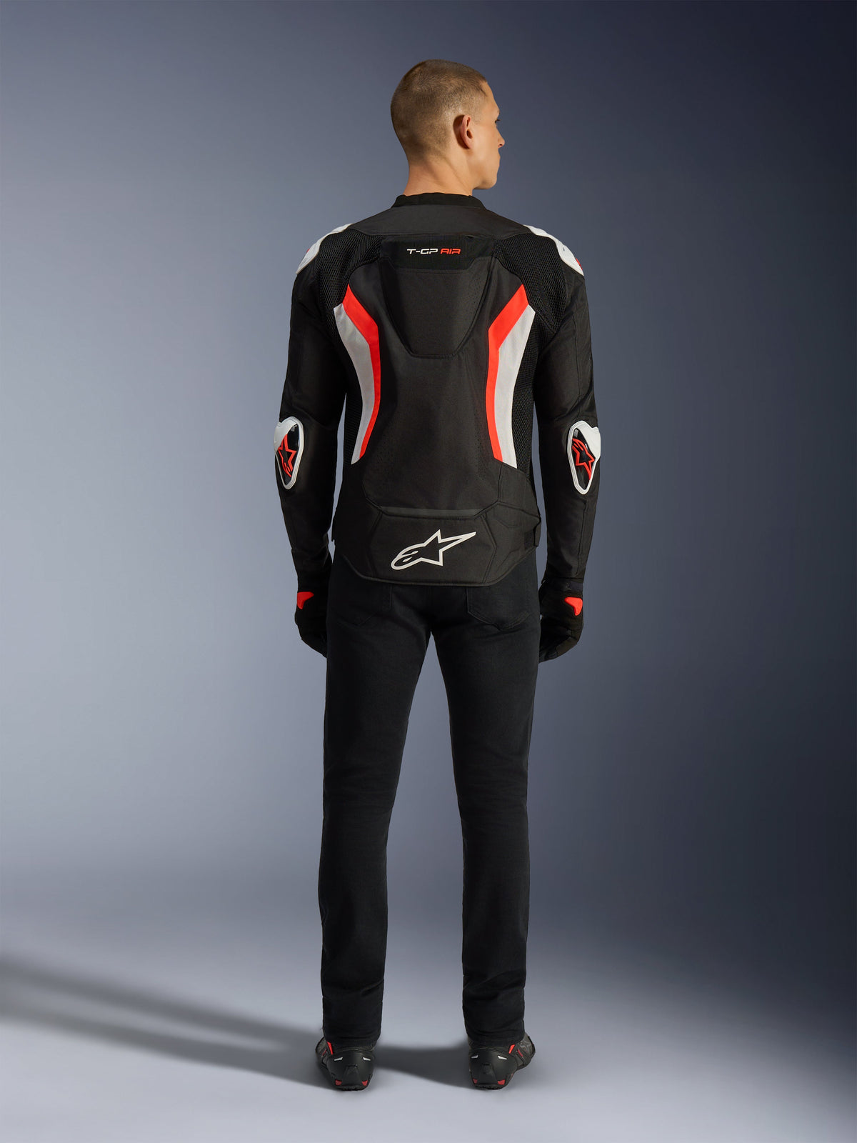 Alpinestars T-GP Air Jacket, Motorcycle Jacket, Black Red Fluo, rear view on a model, featuring an aerodynamic hump, white and fluorescent red accents, Alpinestars logo on the lower back, sport-cut design for road riding.