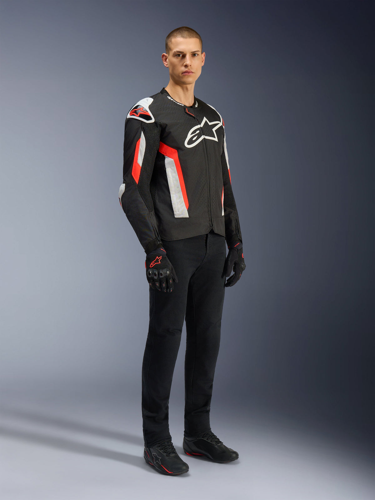 Alpinestars T-GP Air Jacket, Black Red Fluo, worn by model with black riding pants and gloves, featuring laser-perforated textile panels, white Alpinestars branding, and red accents, sport motorcycle jacket for warm weather road riding